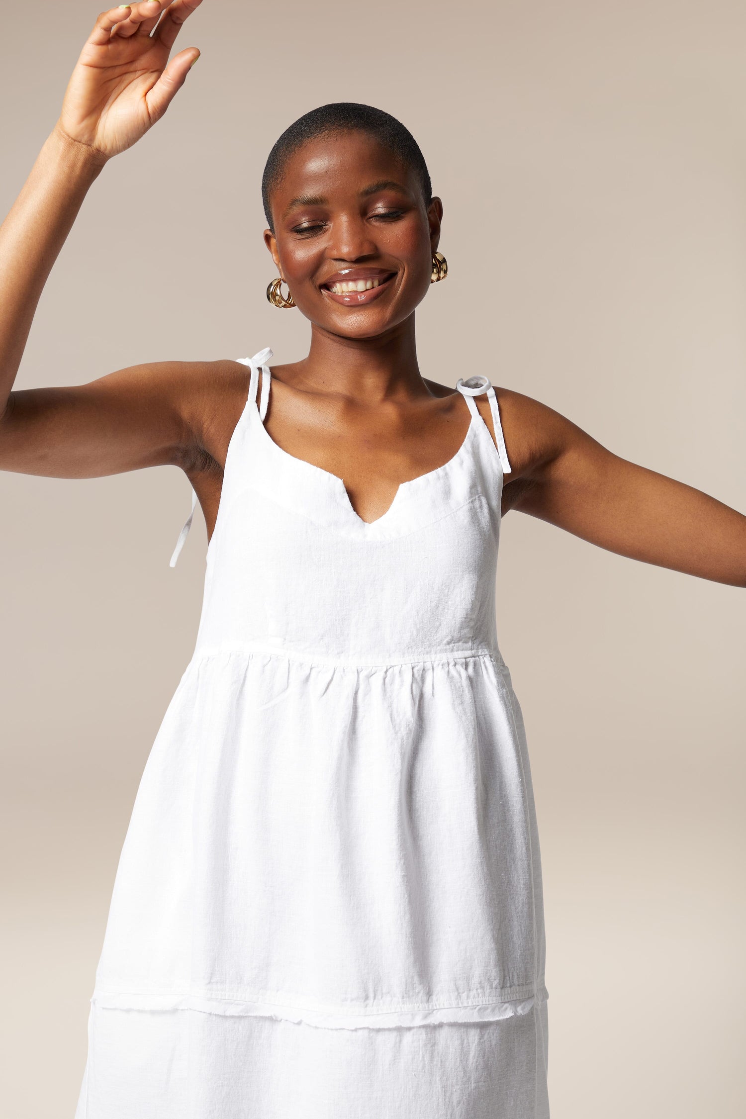 A woman in a Linen Tiered Dress with adjustable shoulder ties, her arms outstretched.