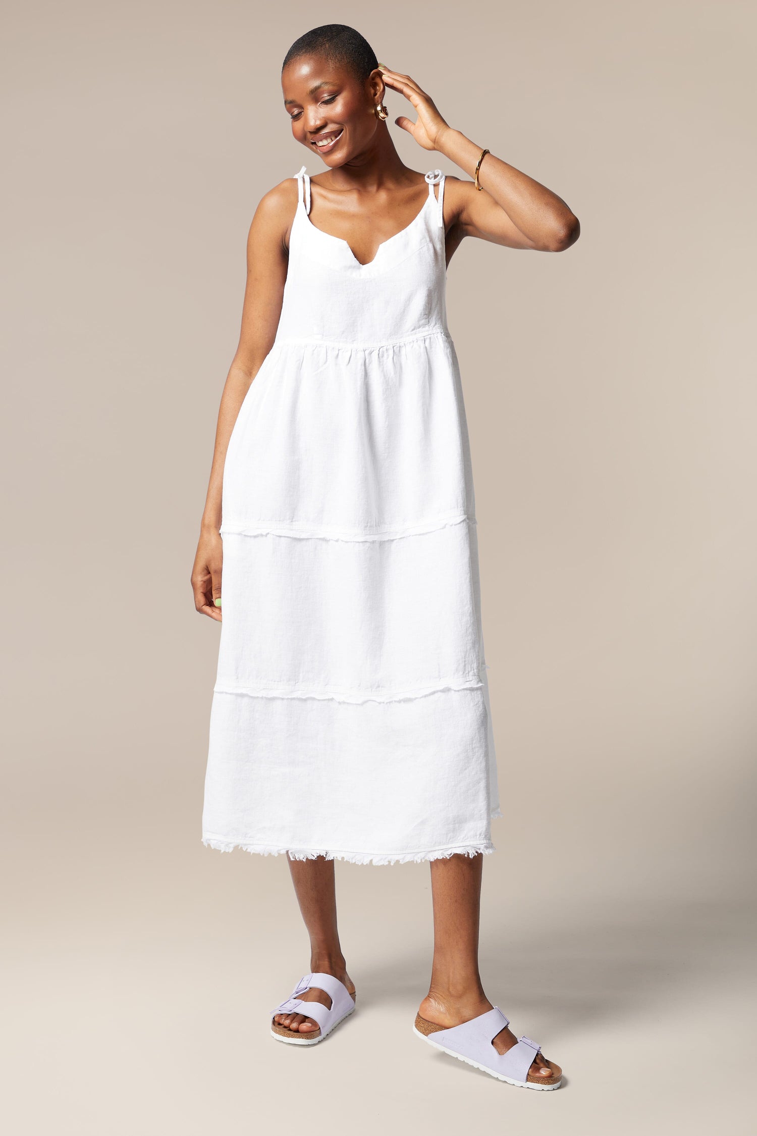 A woman wearing a Linen Tiered Dress with adjustable shoulder ties, a summer staple paired with sandals.