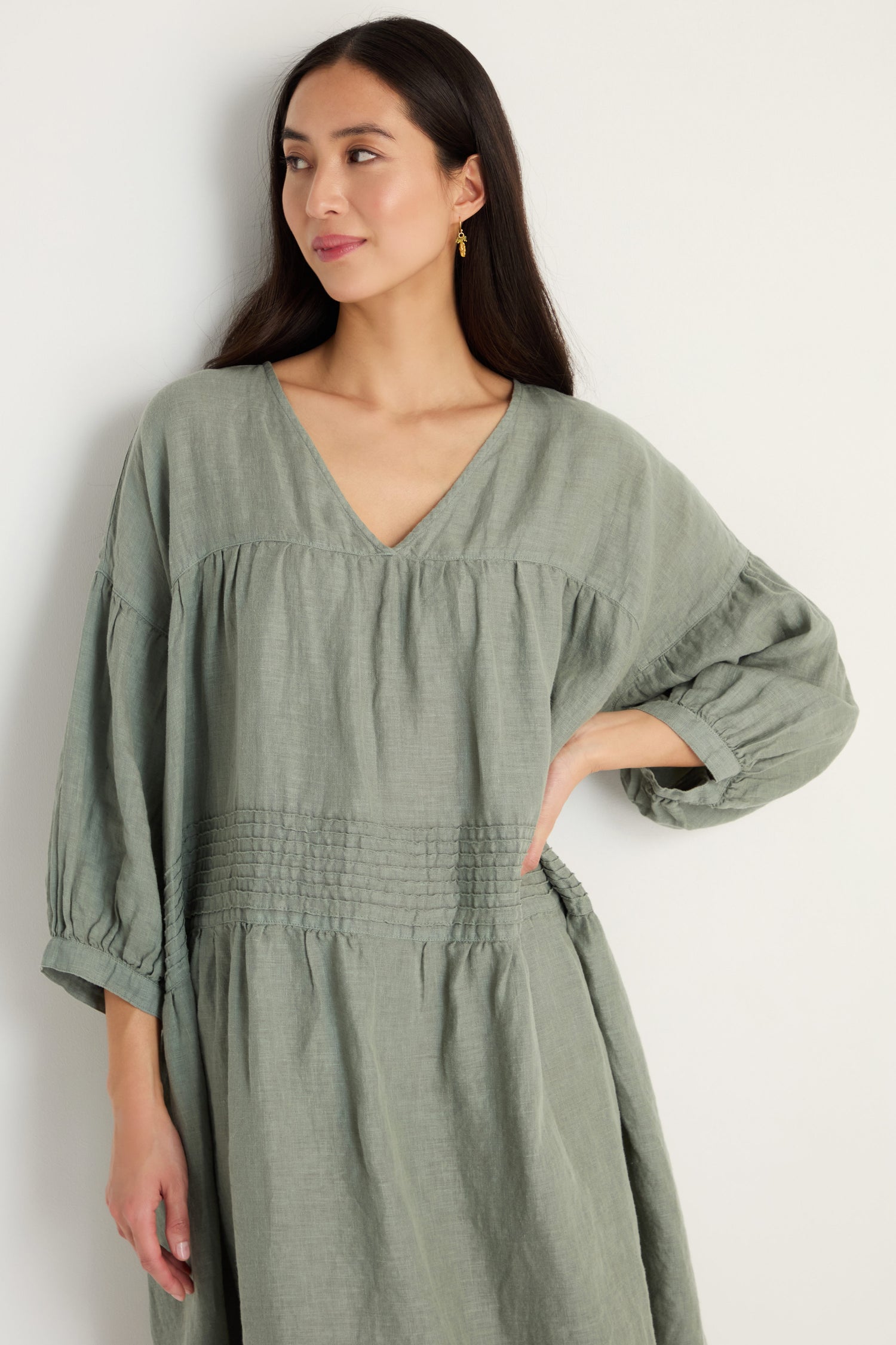 A woman models the Easy Fit V-Neck Sage Linen Dress, featuring long sleeves, against a simple light background.