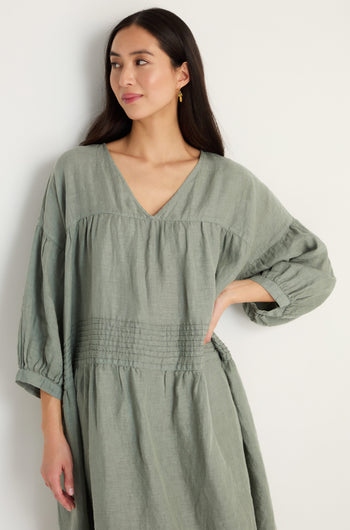A woman models the Easy Fit V-Neck Sage Linen Dress, featuring long sleeves, against a simple light background.