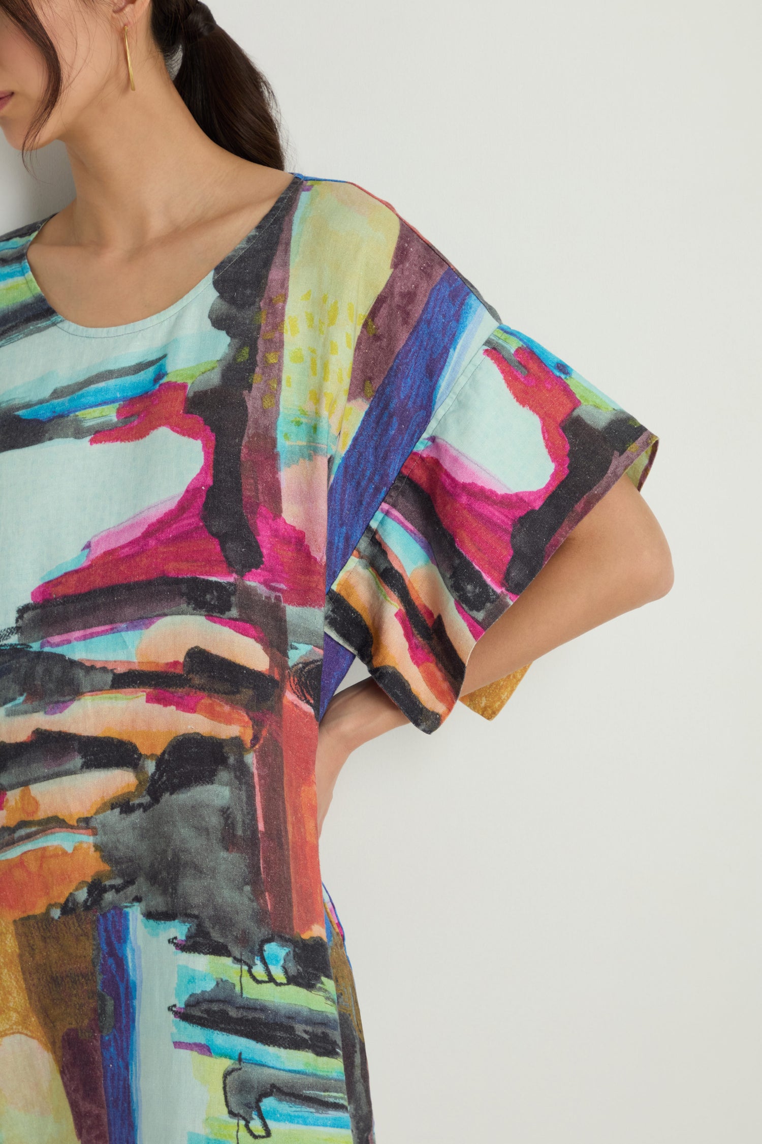 A woman stands against a plain background wearing the Abstract Print Easy Dress, featuring a relaxed silhouette and colorful abstract pattern, paired with black sandals.
