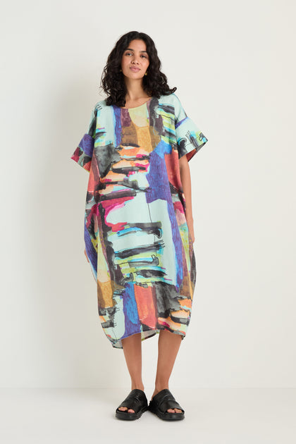 A woman stands against a plain background wearing the Abstract Print Easy Dress, featuring a relaxed silhouette and colorful abstract pattern, paired with black sandals.