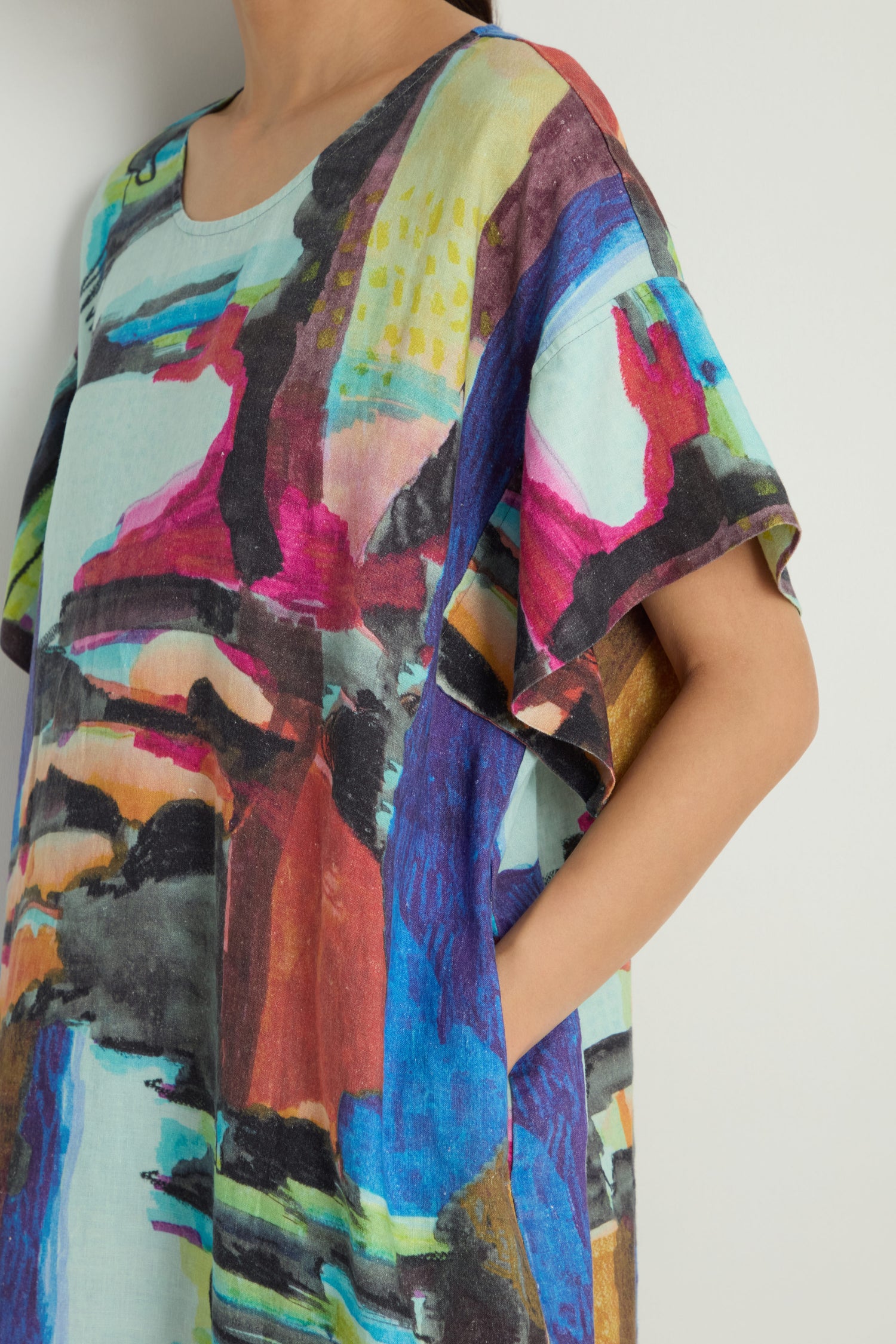 A person’s hand is partially tucked into the pocket of the Abstract Print Easy Dress, a brightly colored linen dress featuring bold abstract patterns.