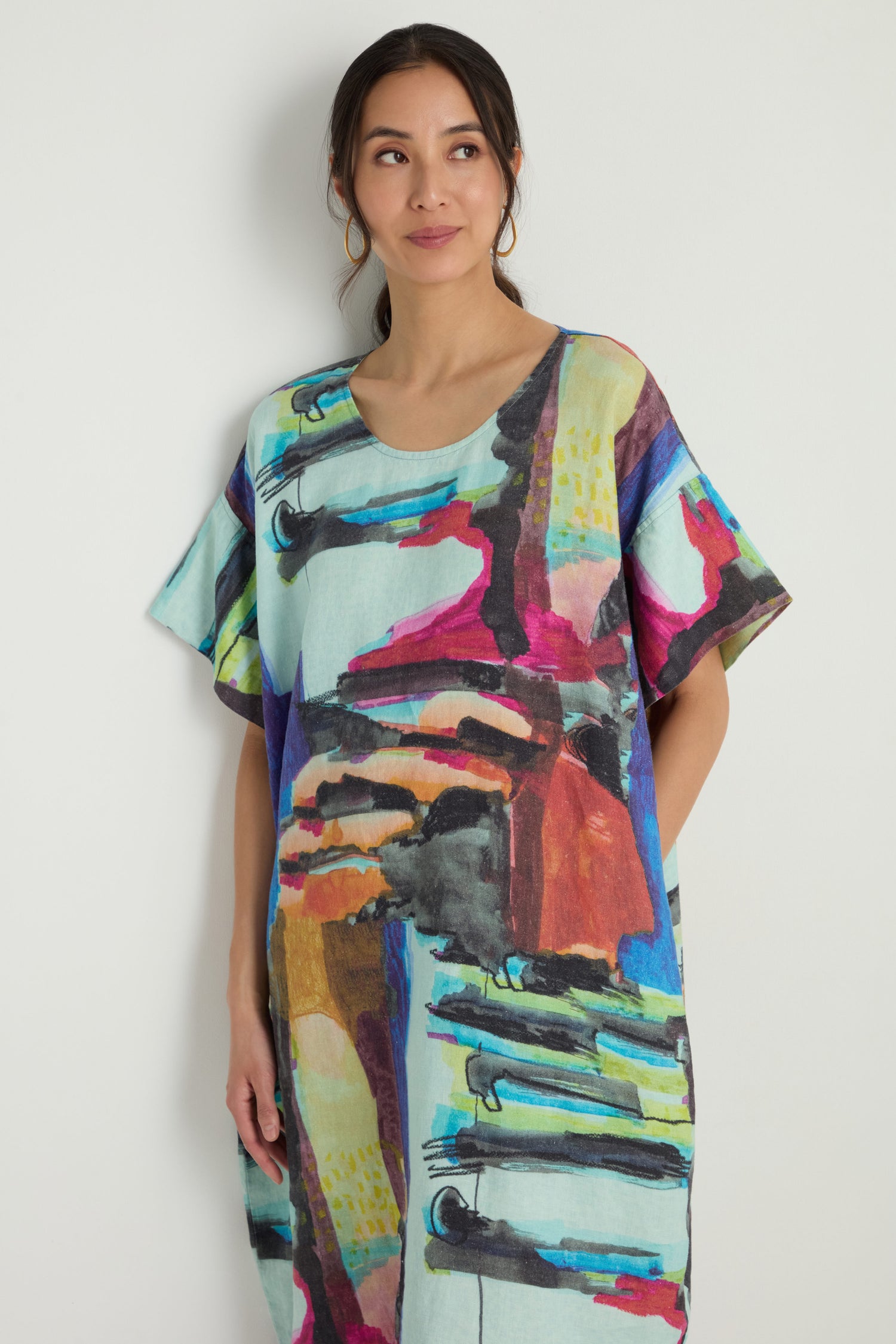A person with wavy hair wears the Abstract Print Easy Dress, featuring a colorful abstract pattern and relaxed silhouette, standing with one hand in their pocket.