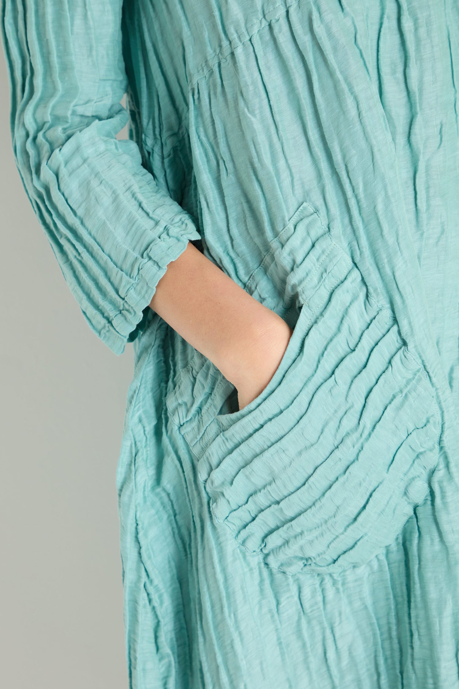 A person with their hand in the pocket of a Silk Linen Mint Patch Pocket Dress, featuring light blue textured crinkled fabric.