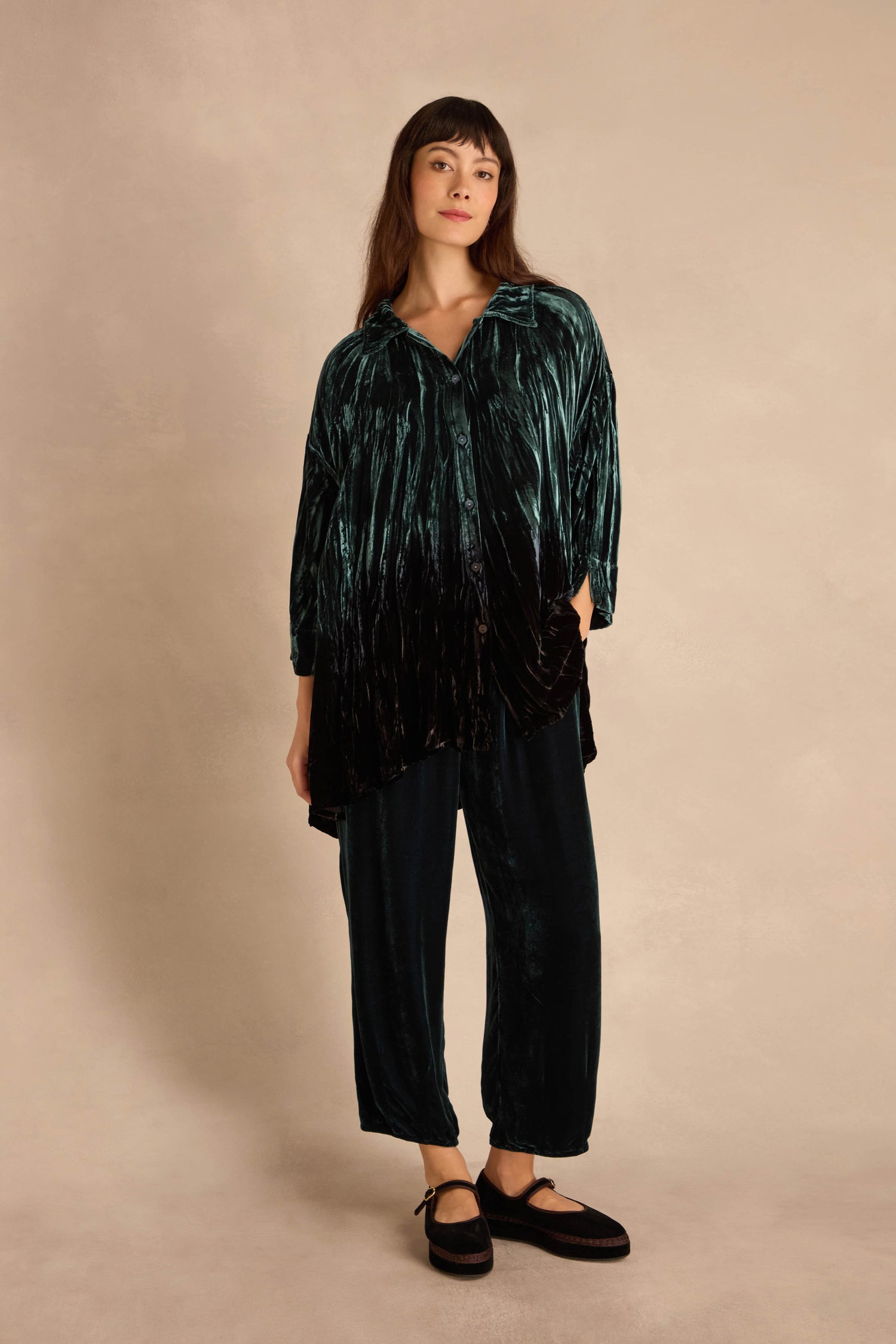 Woman stands against a neutral backdrop wearing the Turquoise Silk Velvet Ombre Shirt with matching pants and black shoes.