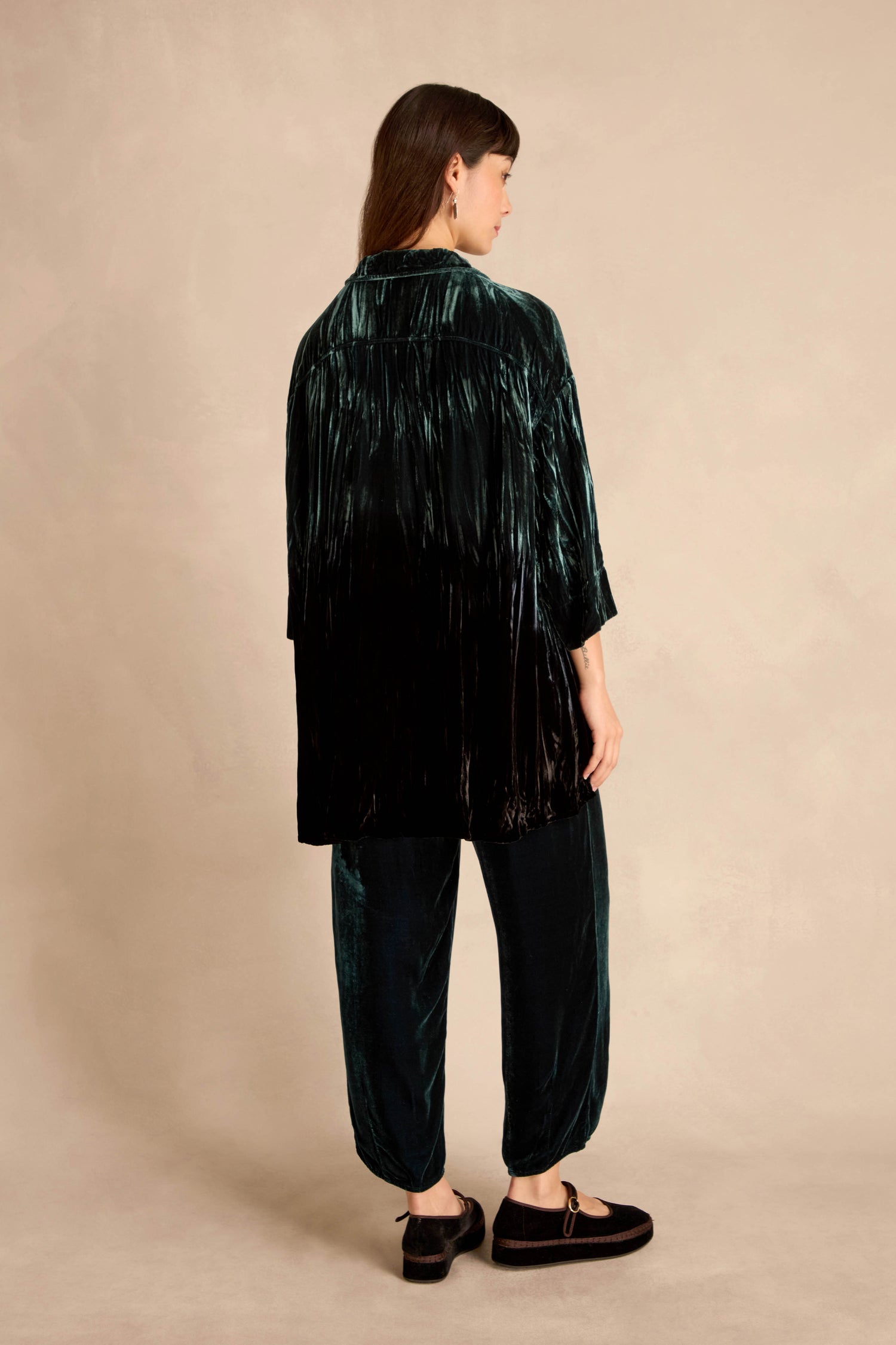 A woman faces away, wearing the Turquoise Silk Velvet Ombre Shirt with matching pants and black flats, in front of a plain beige background.