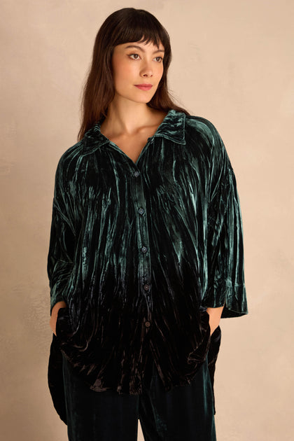 Woman wearing a loose, Turquoise Silk Velvet Ombre Shirt with hands in pockets, standing against a neutral background.