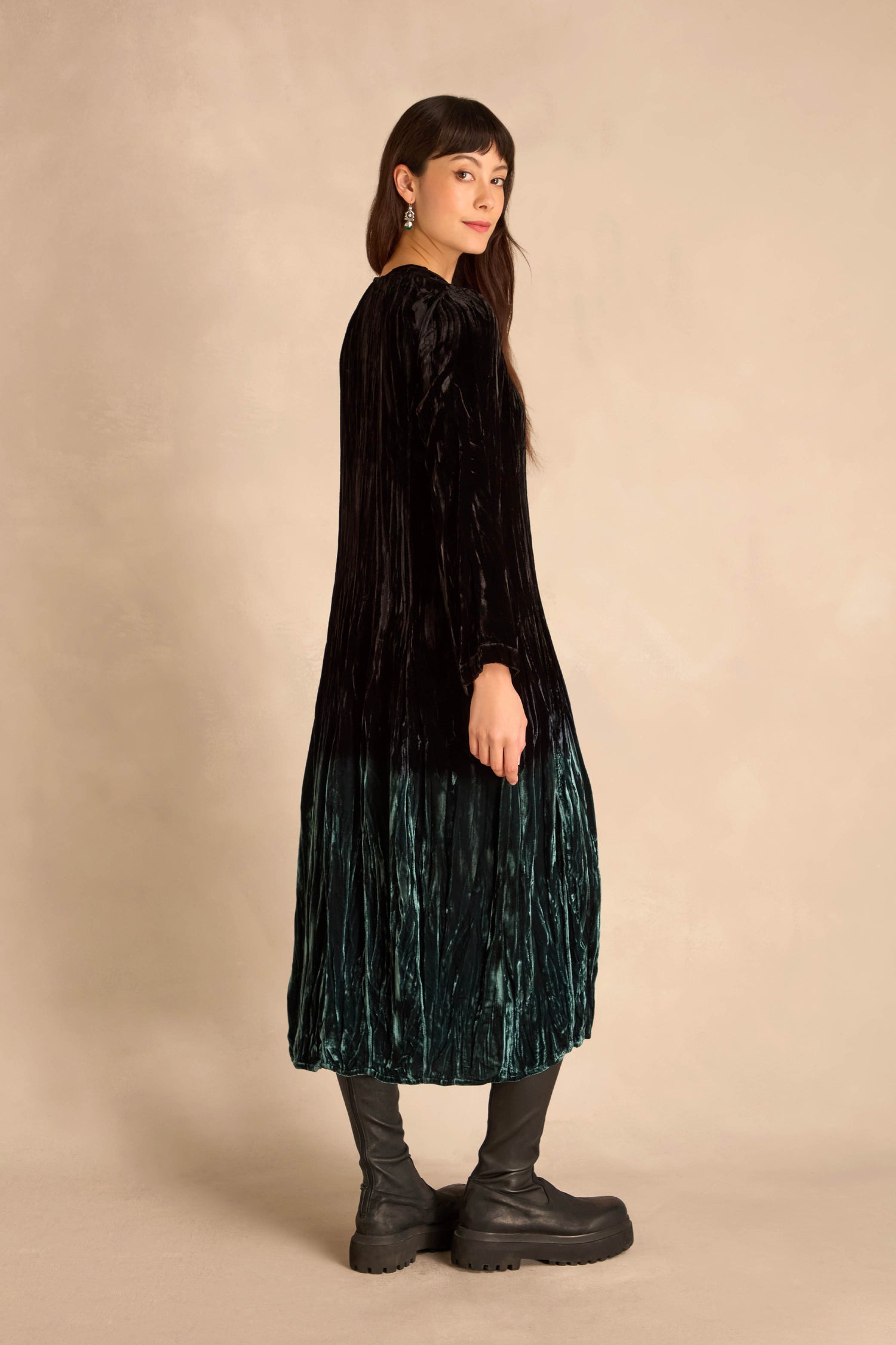Person standing sideways in the Silk Velvet Ombre Bubble Dress with black boots, set against a beige background.