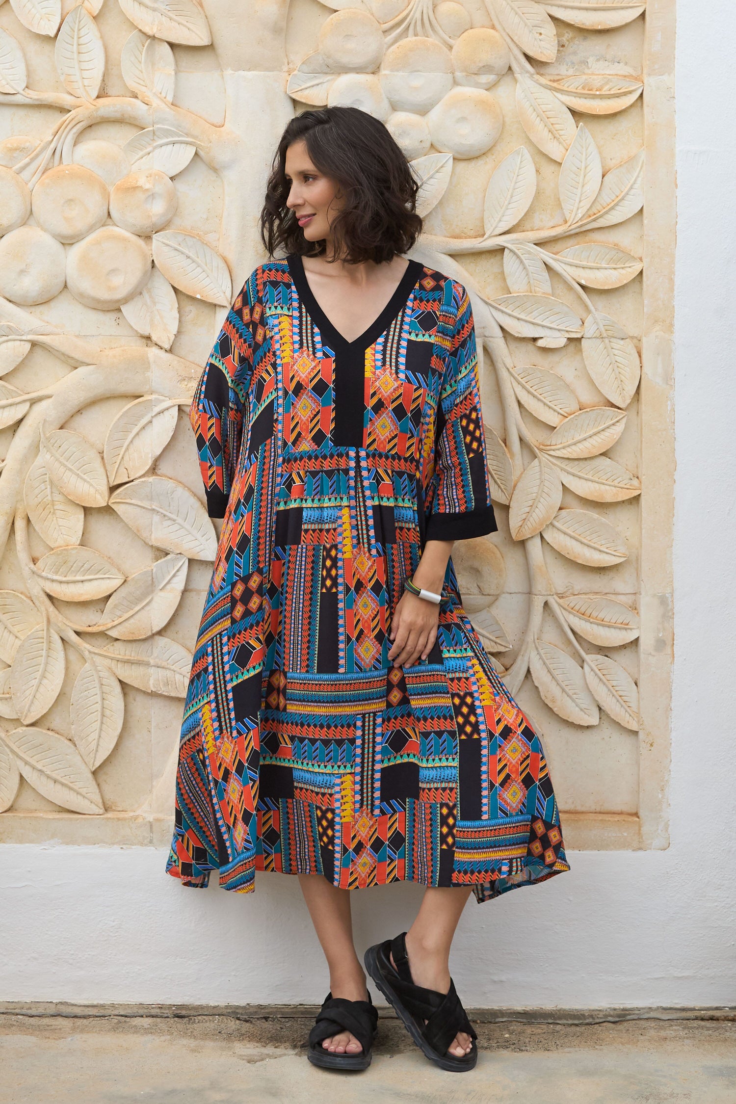 A woman wearing a Bold Graphic Printed Dress with vibrant pattern in front of a wall.