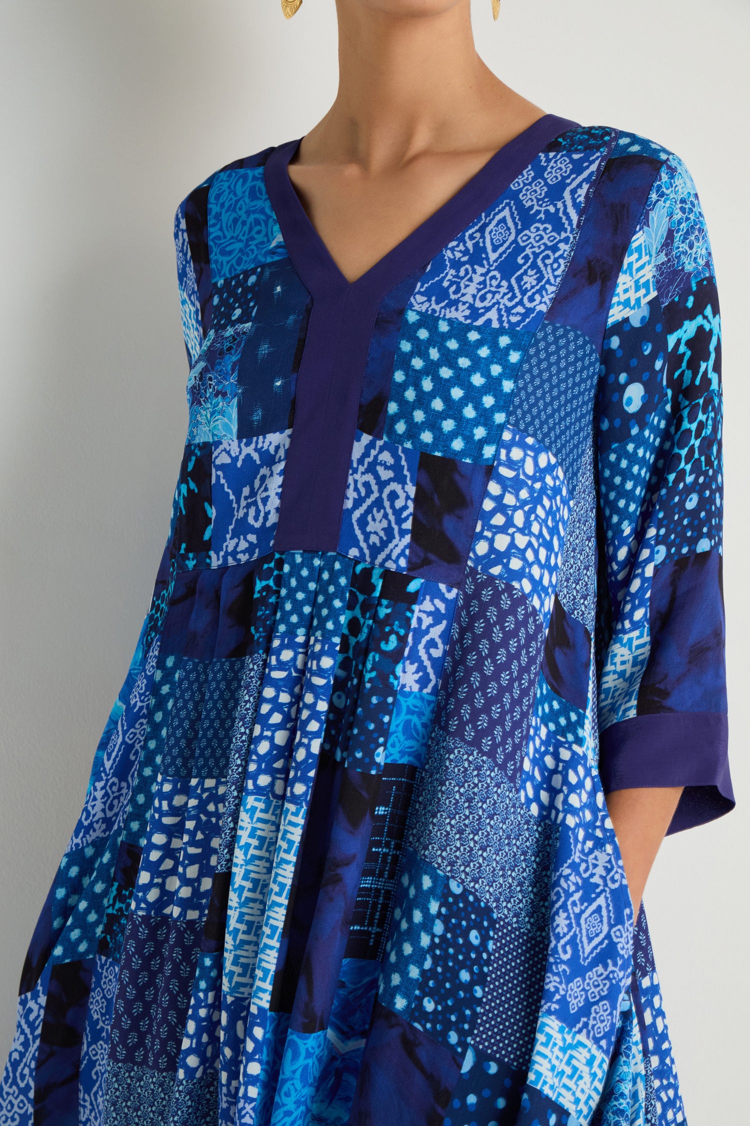 A woman wears the Sahara Indigo Patchwork Flared Dress, featuring three-quarter sleeves, a flared silhouette, and blue geometric and abstract designs on viscose crepe.