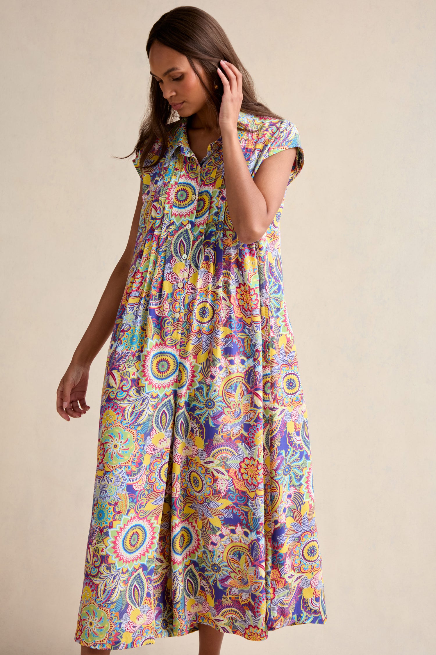 A woman stands against a plain background wearing the Summer Sarasa Jumpsuit, a sleeveless, button-down piece featuring a vibrant paisley and floral pattern.