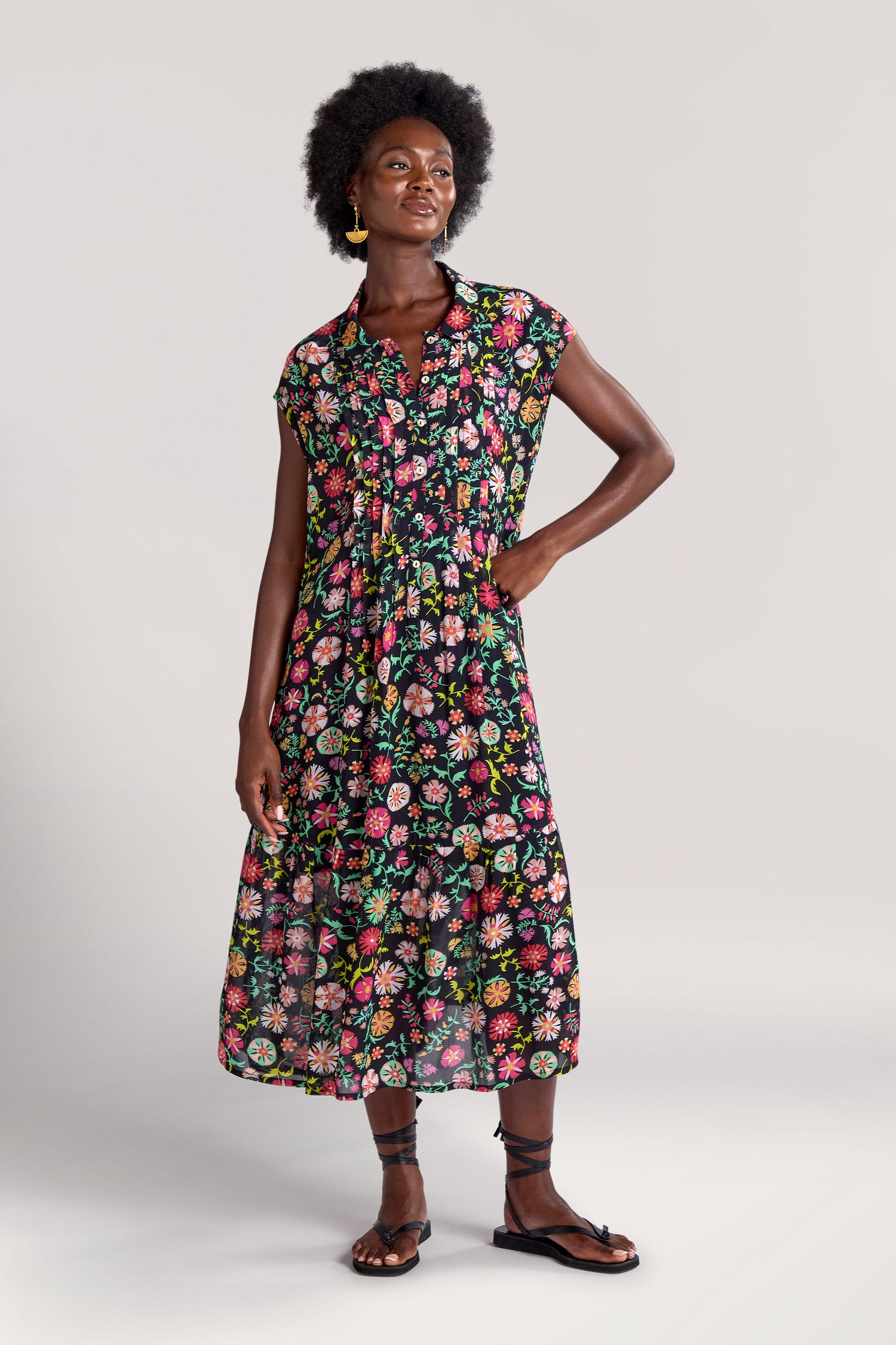 Person wearing a Folkloric Floral Shirt Dress with a colorful floral print, yellow earrings, and black sandals, standing against a plain light background.