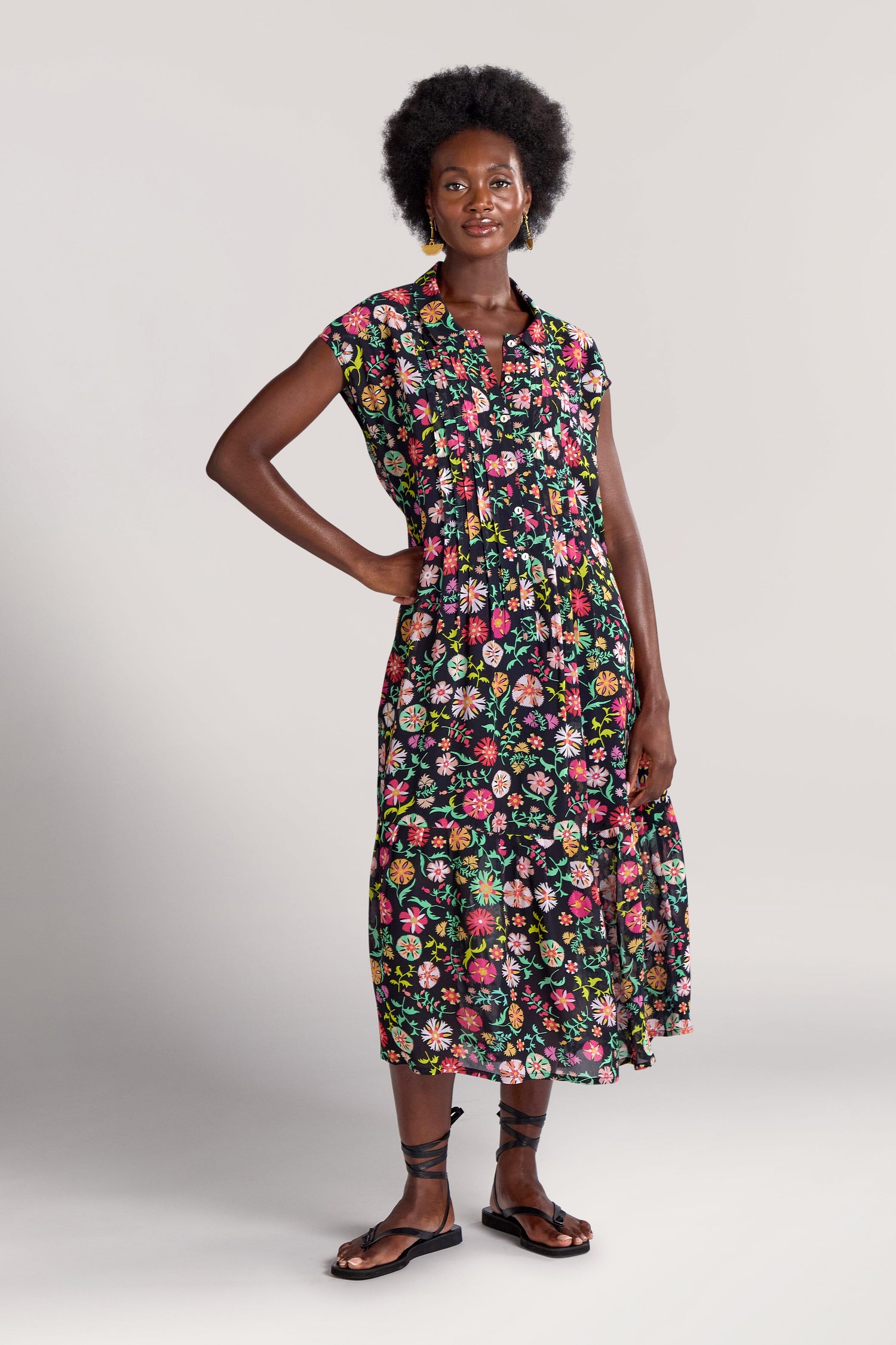 A person stands confidently wearing a Folkloric Floral Shirt Dress paired with black sandals, against a plain background.