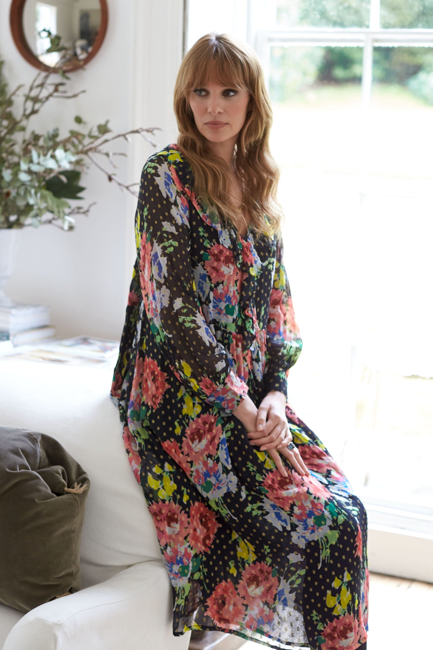 A woman in a free-flowing fit Floral Bouquet Frill Dress, sitting on a couch adorned with a print of flowers and polka dots wore the Floral Bouquet Frill Dress.