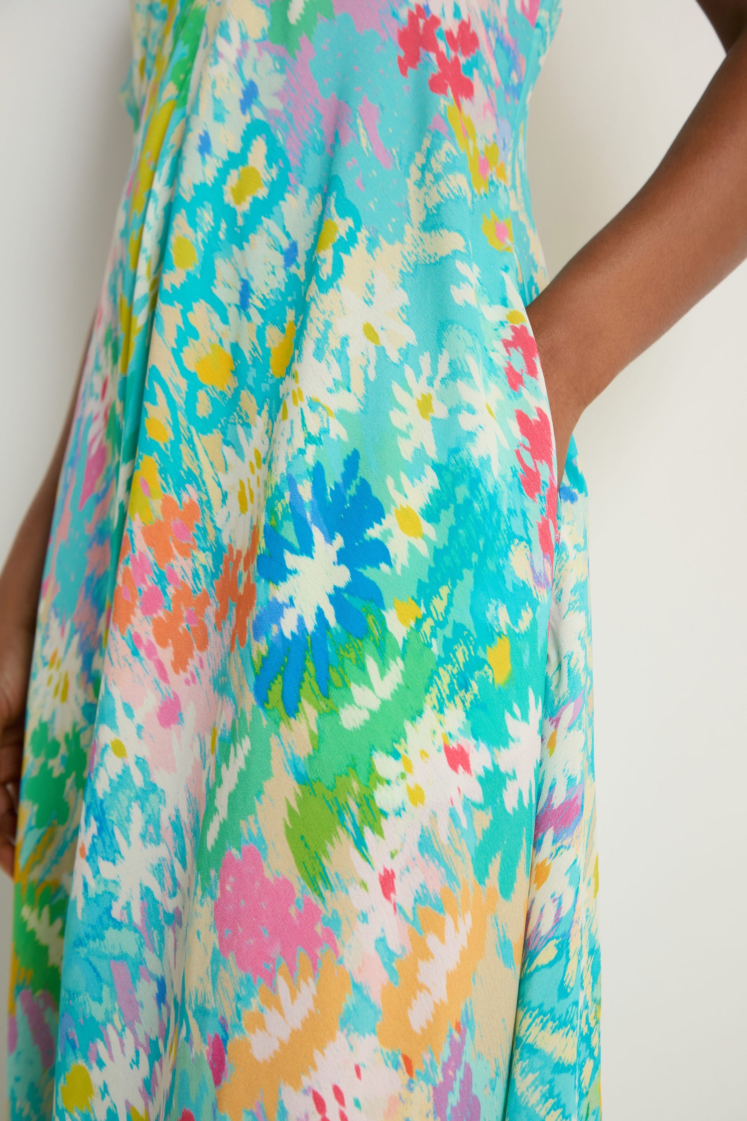 Close-up of a person wearing the Floral Oasis Maxi Dress, highlighting its colorful abstract floral design in soft viscose crepe; their hand is placed in the side pocket.