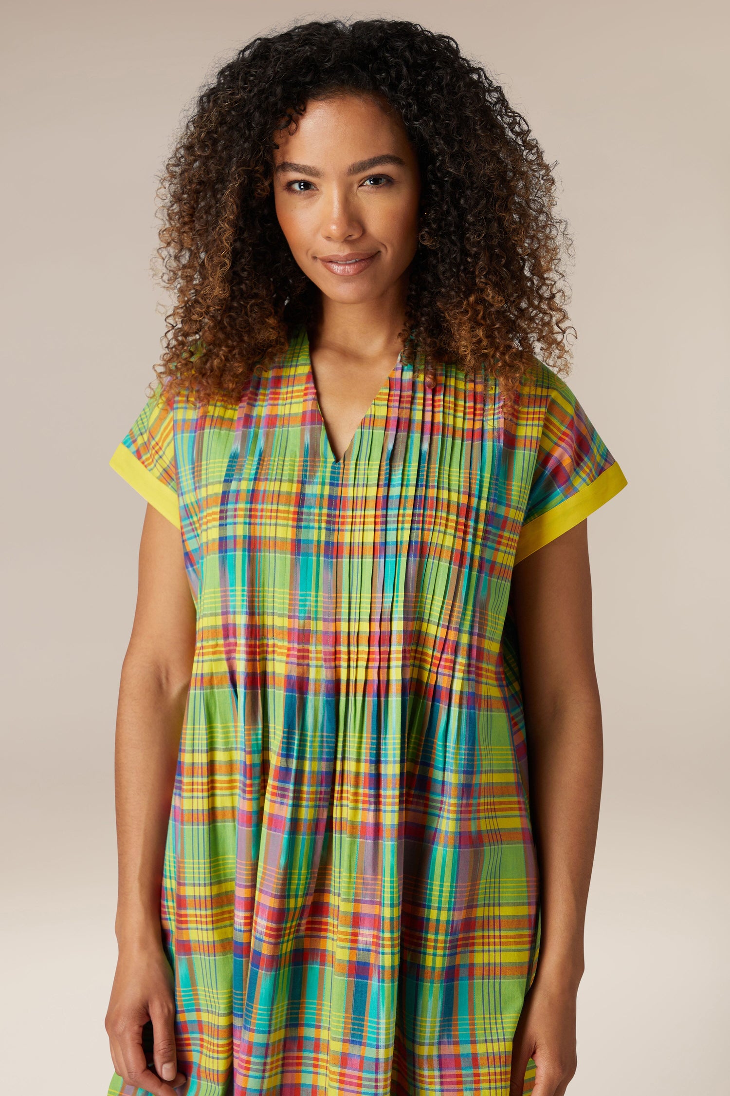 A woman with curly hair smiling in a Multicoloured Ikat Check Dress, standing against a neutral background.