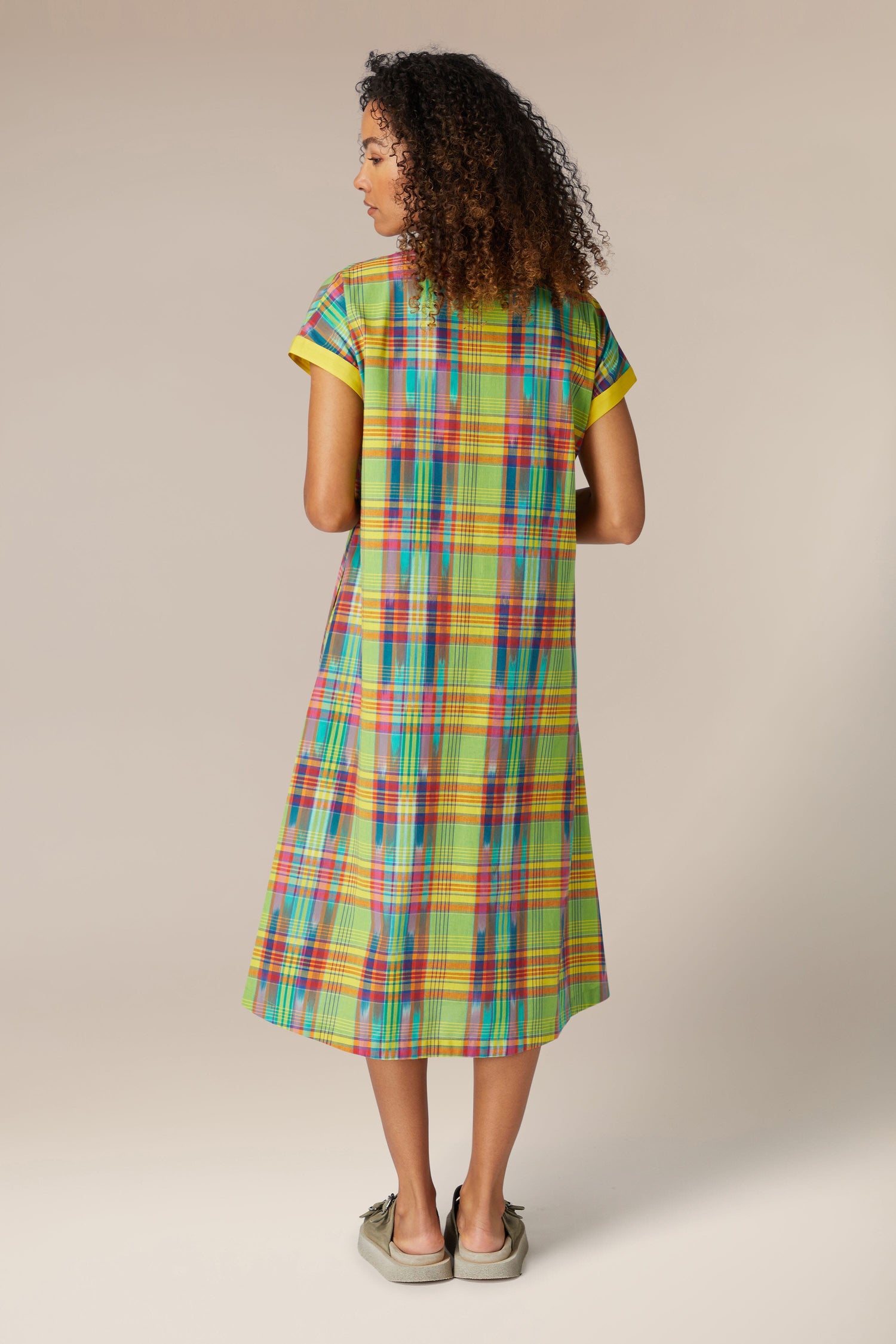 Woman from behind, wearing a Multicoloured Ikat Check Dress and sneakers, standing against a neutral background.