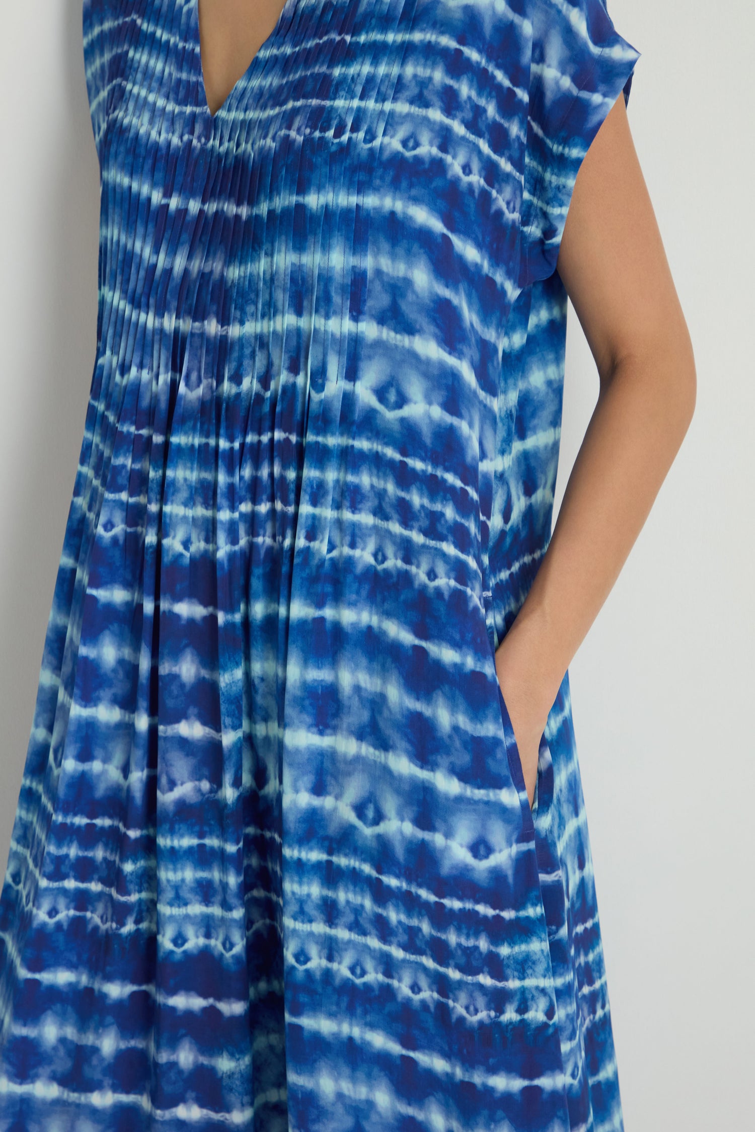 A person wearing the Tie Dye Printed Viscose Pleated Dress with short sleeves, standing with one hand in a pocket.