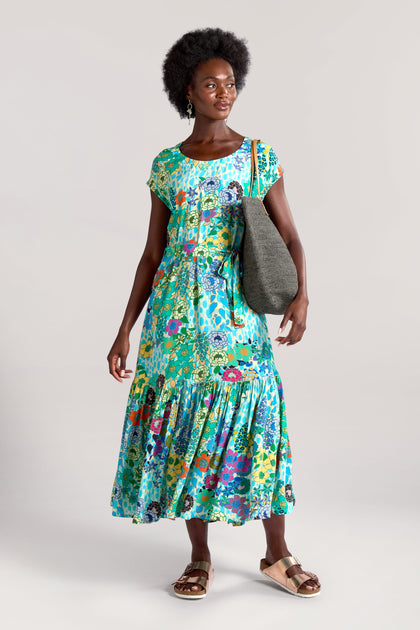 A person wearing a Garden Spot Frill Hem Maxi Dress, gold sandals, and holding a gray tote bag stands against a plain background.