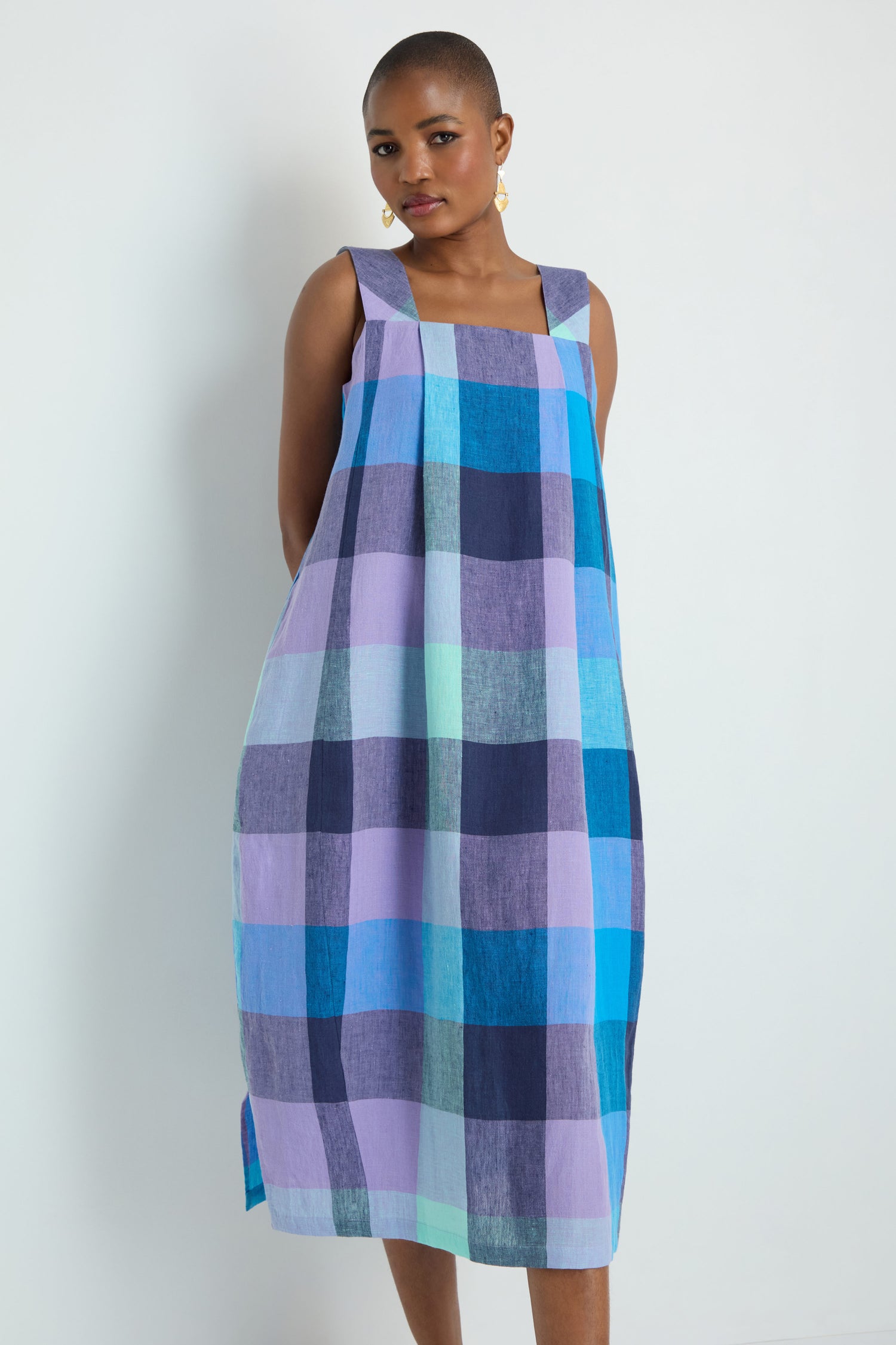 Person wearing the Cross Dye Check Linen Bubble Dress, a sleeveless, loose-fitting dress featuring a bold blue, purple, and turquoise plaid pattern, standing against a plain light background.