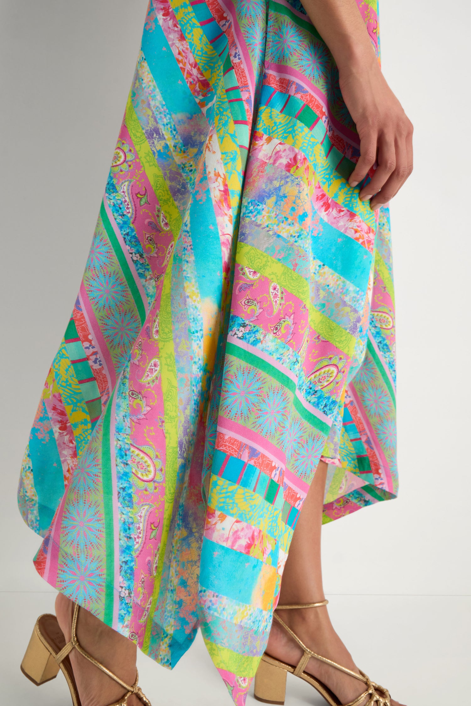 A person in the Patchwork Stripe Summer Dress, featuring colorful stripes in viscose crepe, and gold high-heeled sandals stands against a plain white background.
