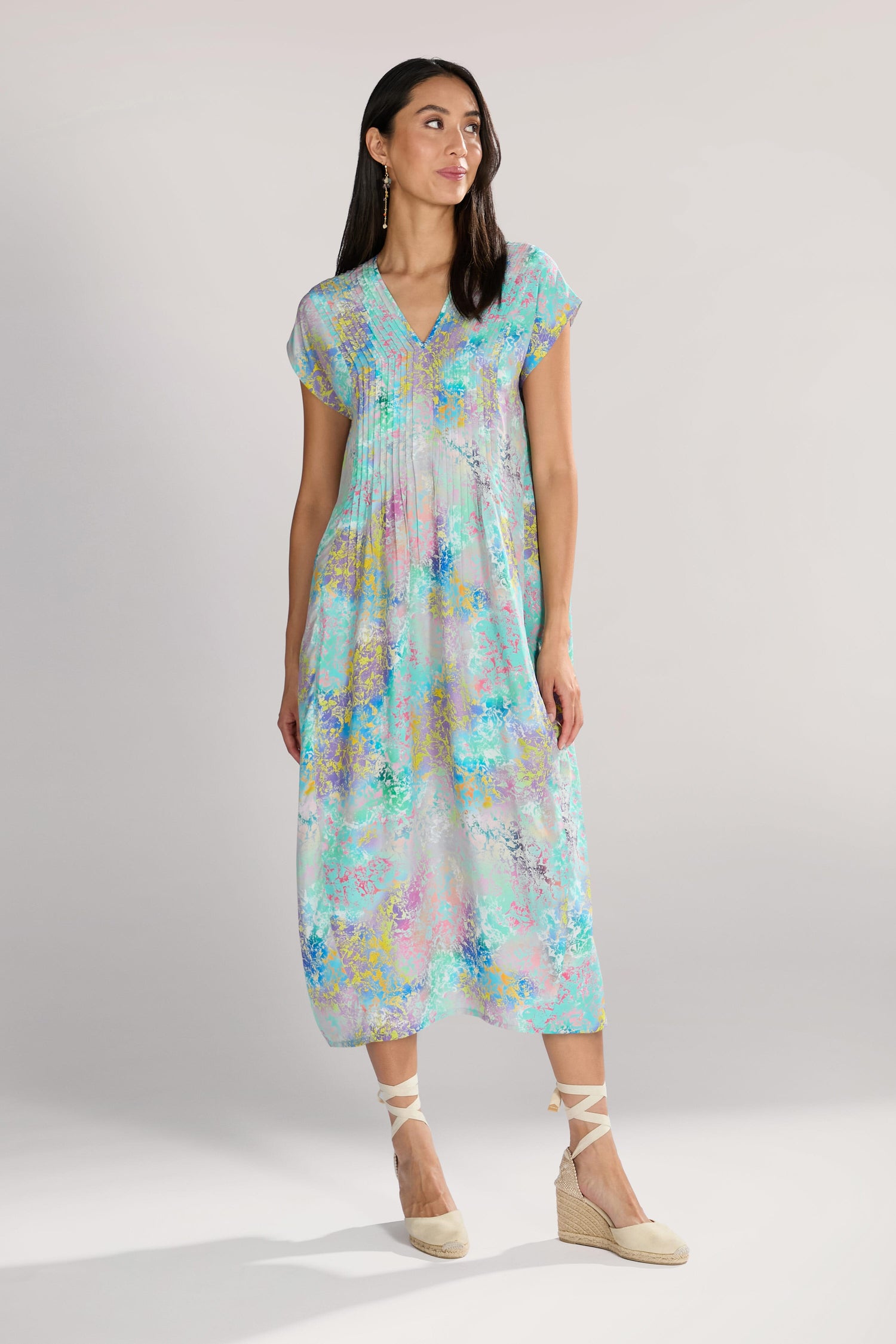 A woman stands wearing an elegant and eye-catching Marbled Cloud Print Bubble Dress with a V-neck and gathered pleats. She complements her look with beige espadrille shoes and earrings, exuding grace as she looks away from the camera.