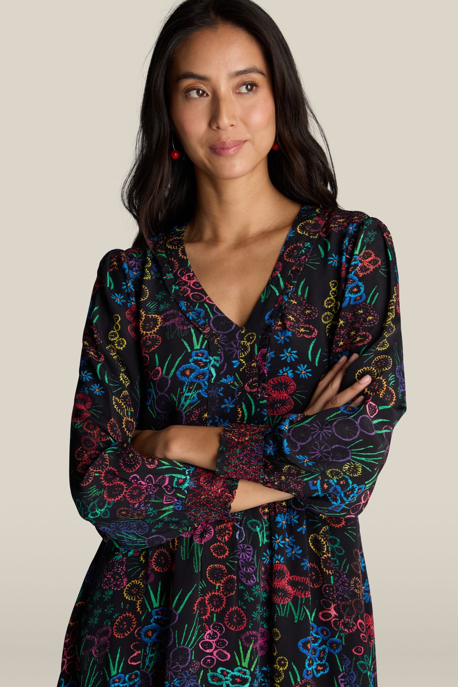 A woman with long dark hair wearing the Embroidered Floral Print Dress stands with her arms crossed against a plain beige background.