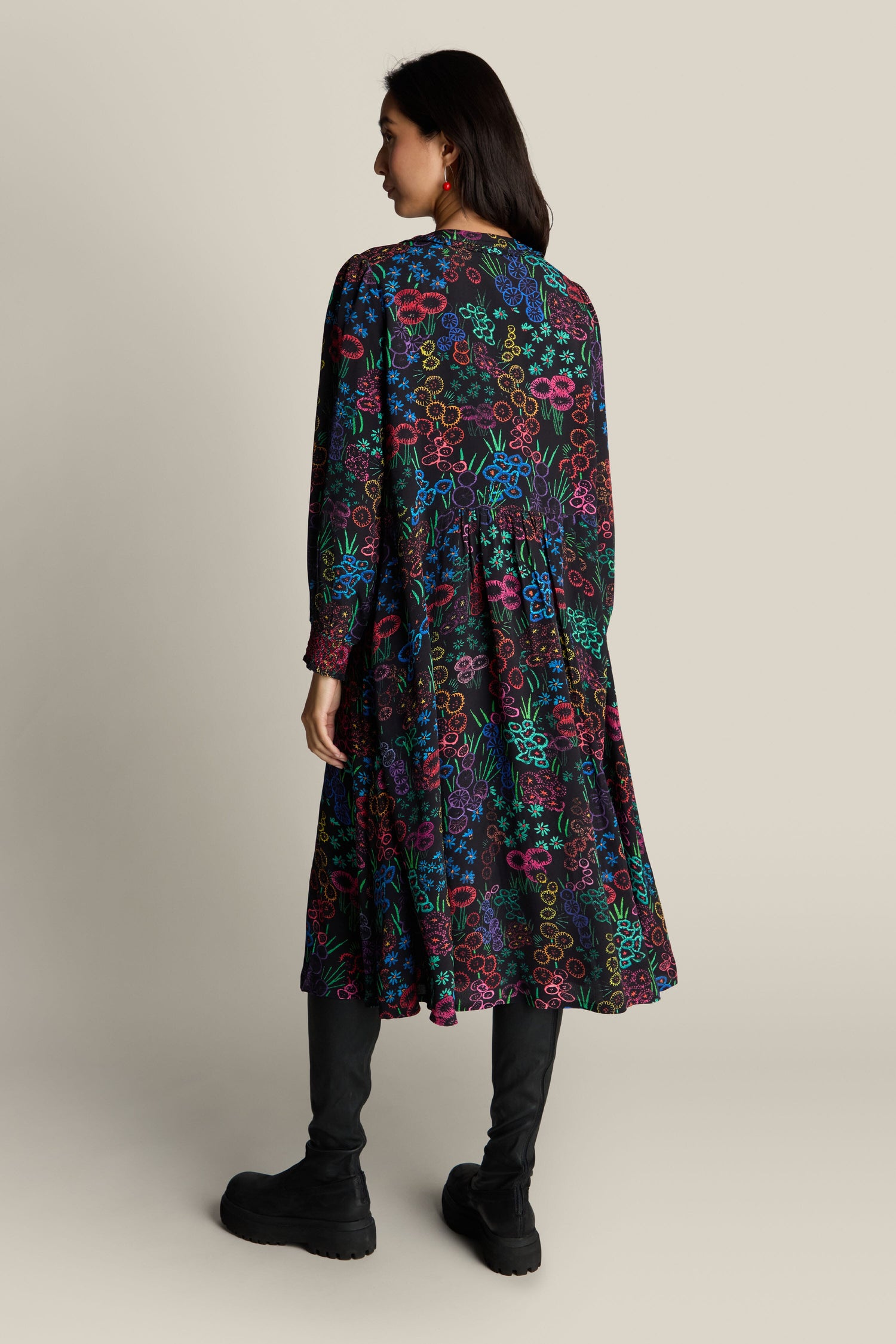 A person wearing the Embroidered Floral Print Dress, featuring intricate floral patterns, stands facing away while sporting black boots.