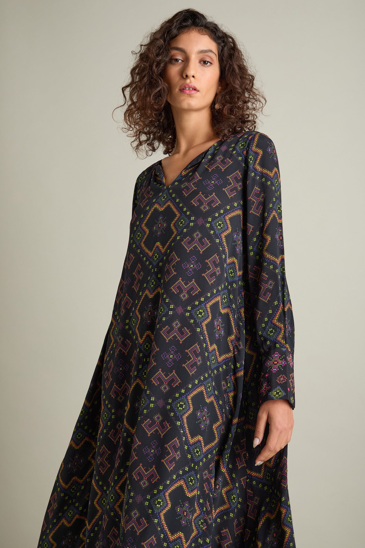 A person with curly hair models the Pixelated Jacquard Print Dress, a long-sleeve garment made of luxurious silky crepe viscose, against a plain background.