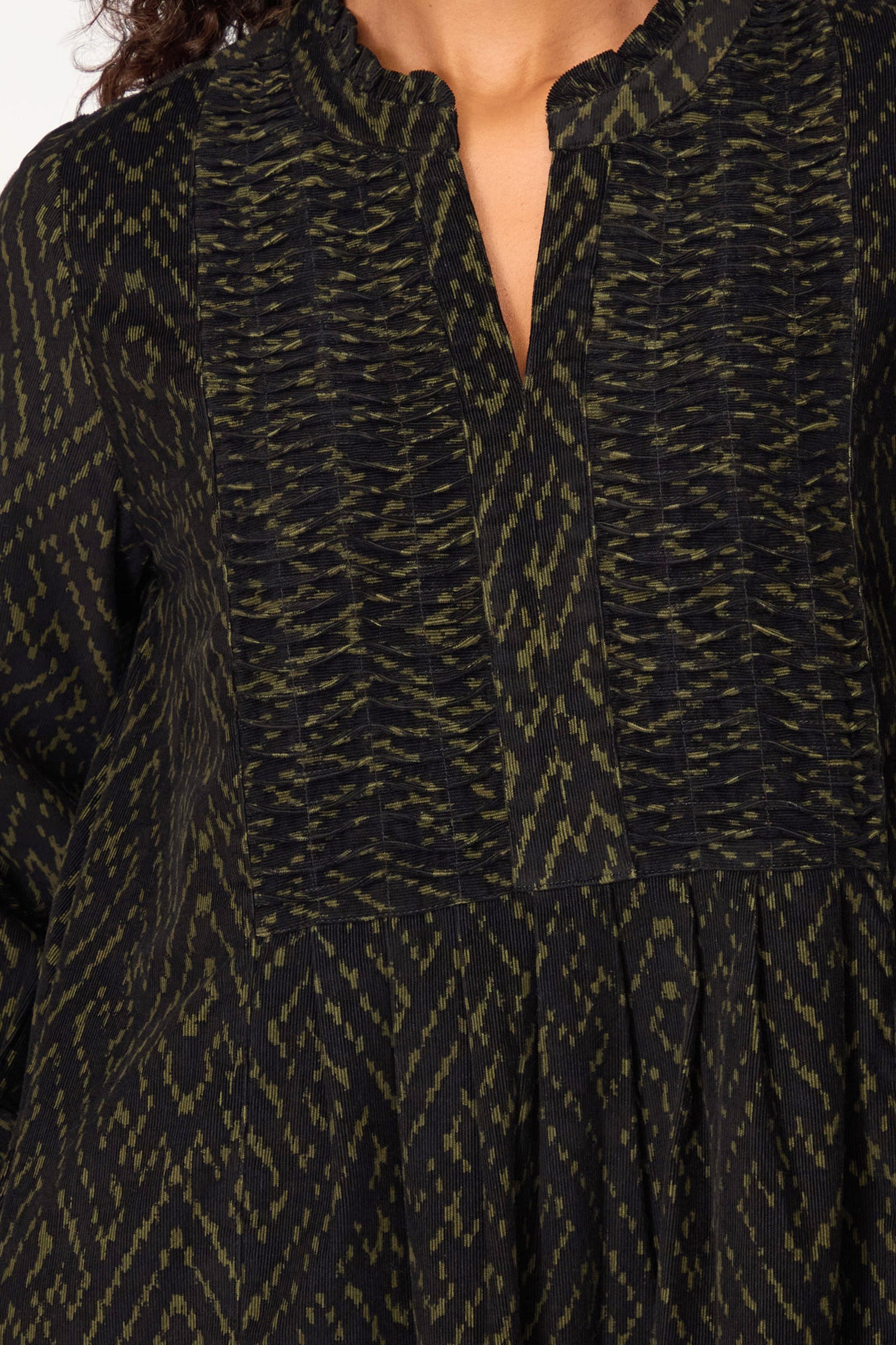 Close-up of a person wearing the Ornate Textured Black and Khaki Cord Dress, featuring a relaxed silhouette and split neckline with an olive green geometric pattern.