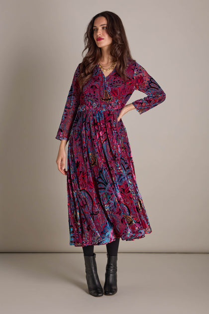 A person stands against a plain background, wearing the Winter Paisley Devore Flared Dress complemented by black boots.