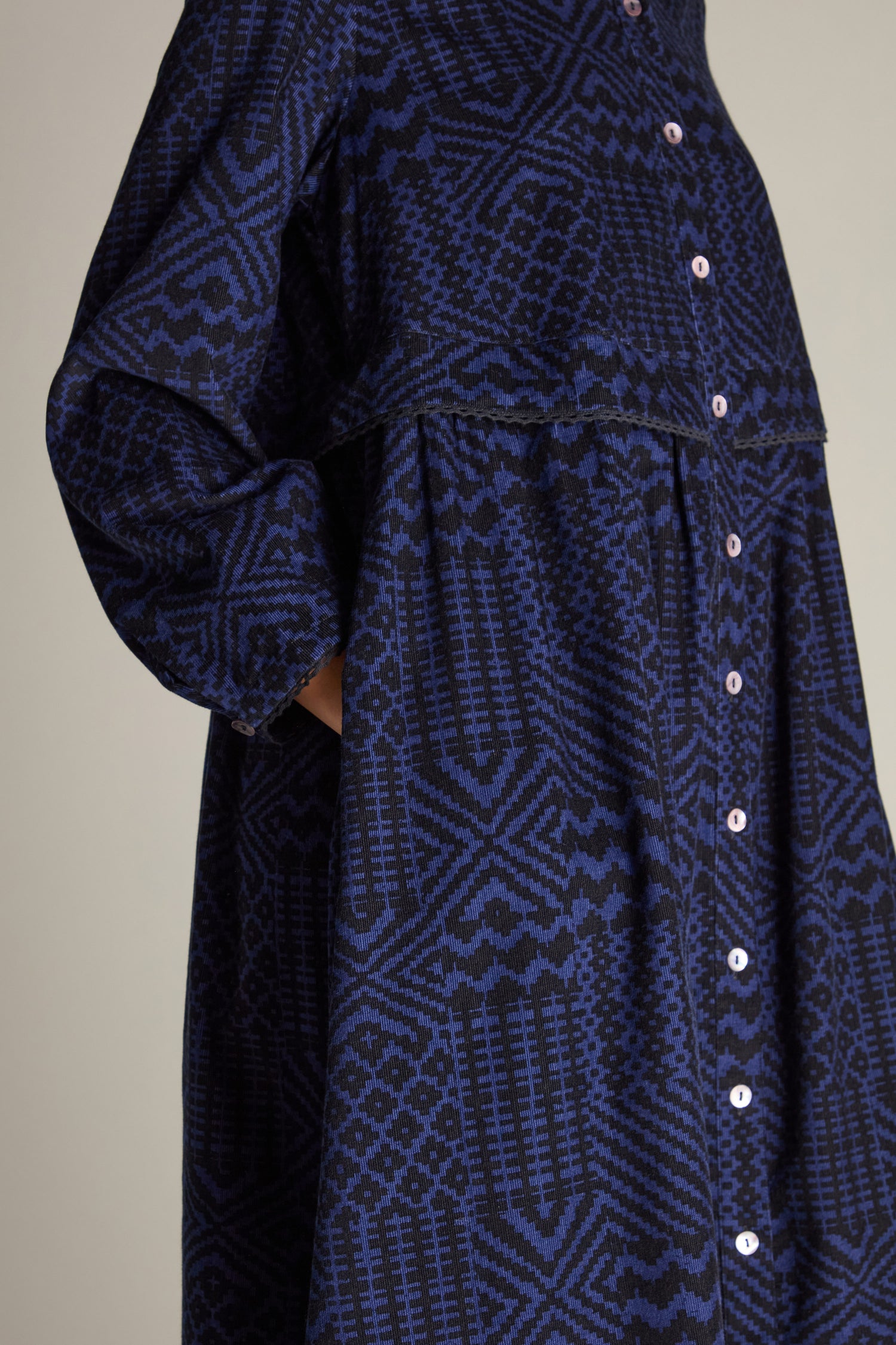 Close-up of a person wearing the Mono Ikat Printed Cord Dress, featuring a dark blue and black patterned button-up design with a high-waist seam, side pockets, and an A-line silhouette inspired by geometric patchwork print.