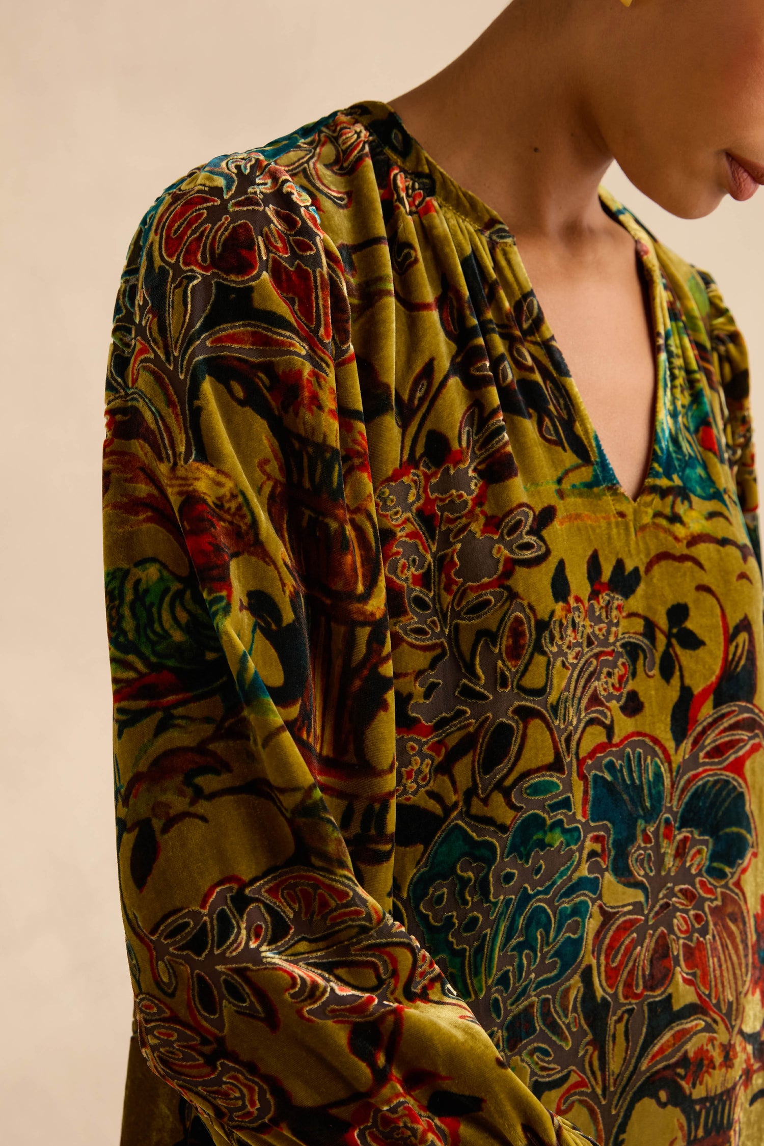A person wearing a Silk Velvet Floral Devore Dress, featuring a v-neck and a multi-colored floral pattern on a dark yellow background.