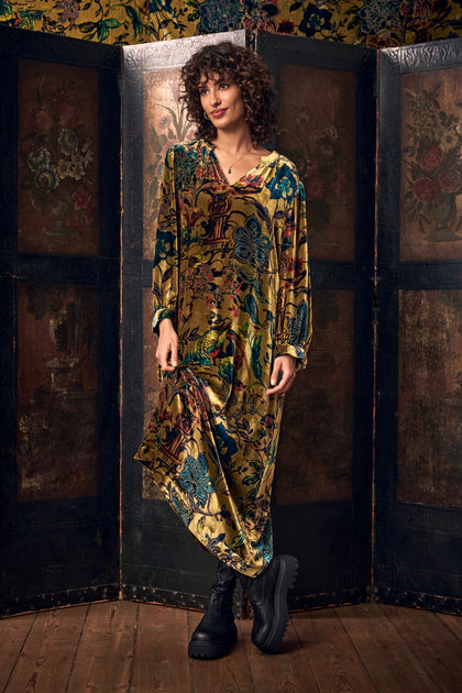 A person wearing a long-sleeved, gold and multicolored Silk Velvet Floral Devore Dress with a baroque print and black chunky-sole boots.