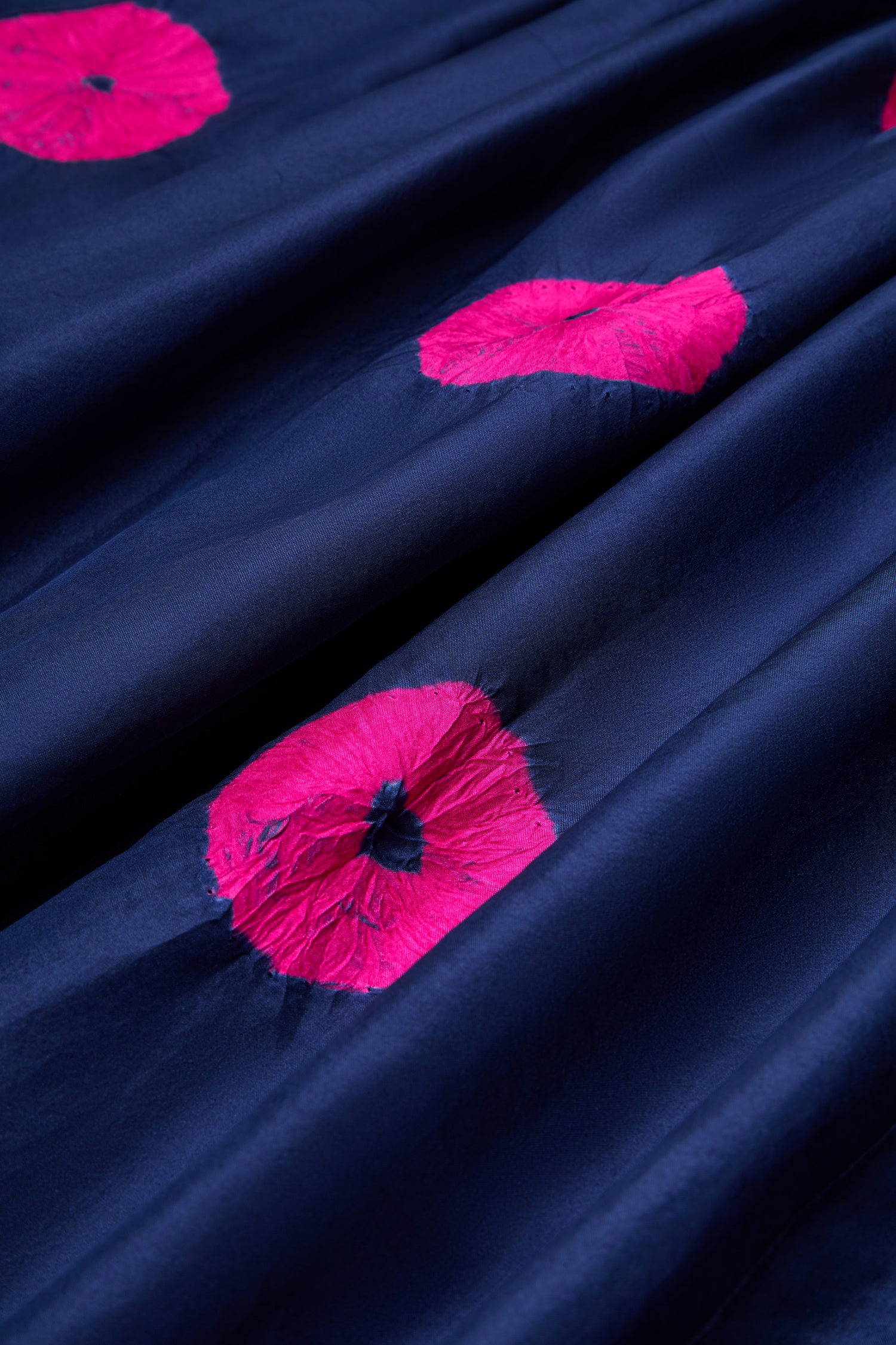 The Shibori Spot Silk Dress features navy blue fabric with pink circular patterns and visible folds, perfect for creating a contemporary silhouette or making a statement.