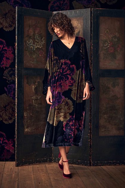 A person wearing the Midnight Peonies Velvet Dress, a long, V-neck midi in a dark floral print, paired with burgundy ankle-strap heels.
