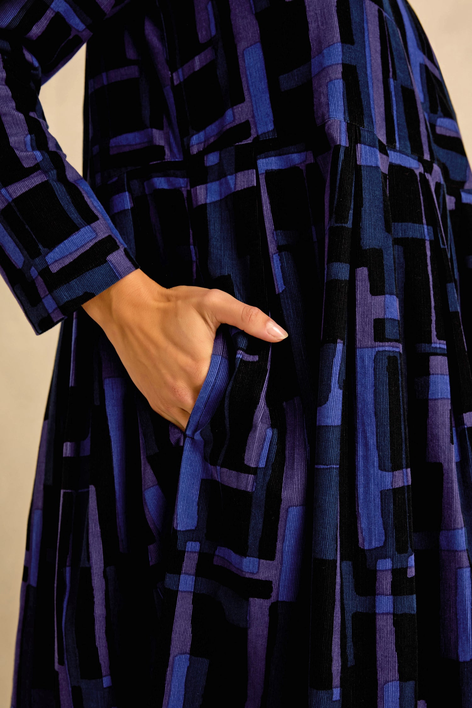 Close-up of a person’s hand in the pocket of the Layered Geometric Cord Flared Dress, a long-sleeved piece featuring a blue and black geometric pattern.