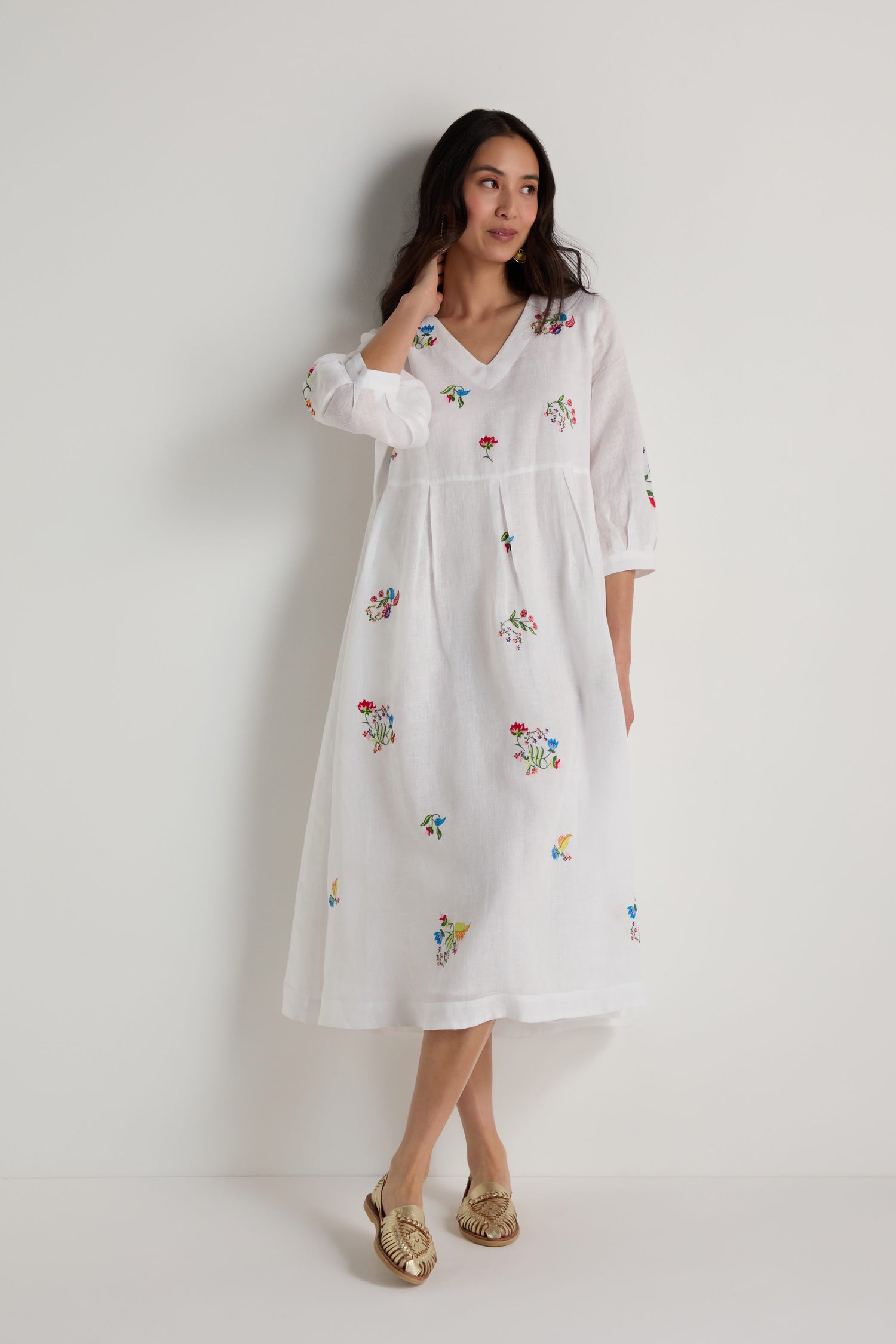 A woman models the Vintage Floral Embroidered Flare Dress, a white linen piece with vibrant floral embroidery, against a plain white background.