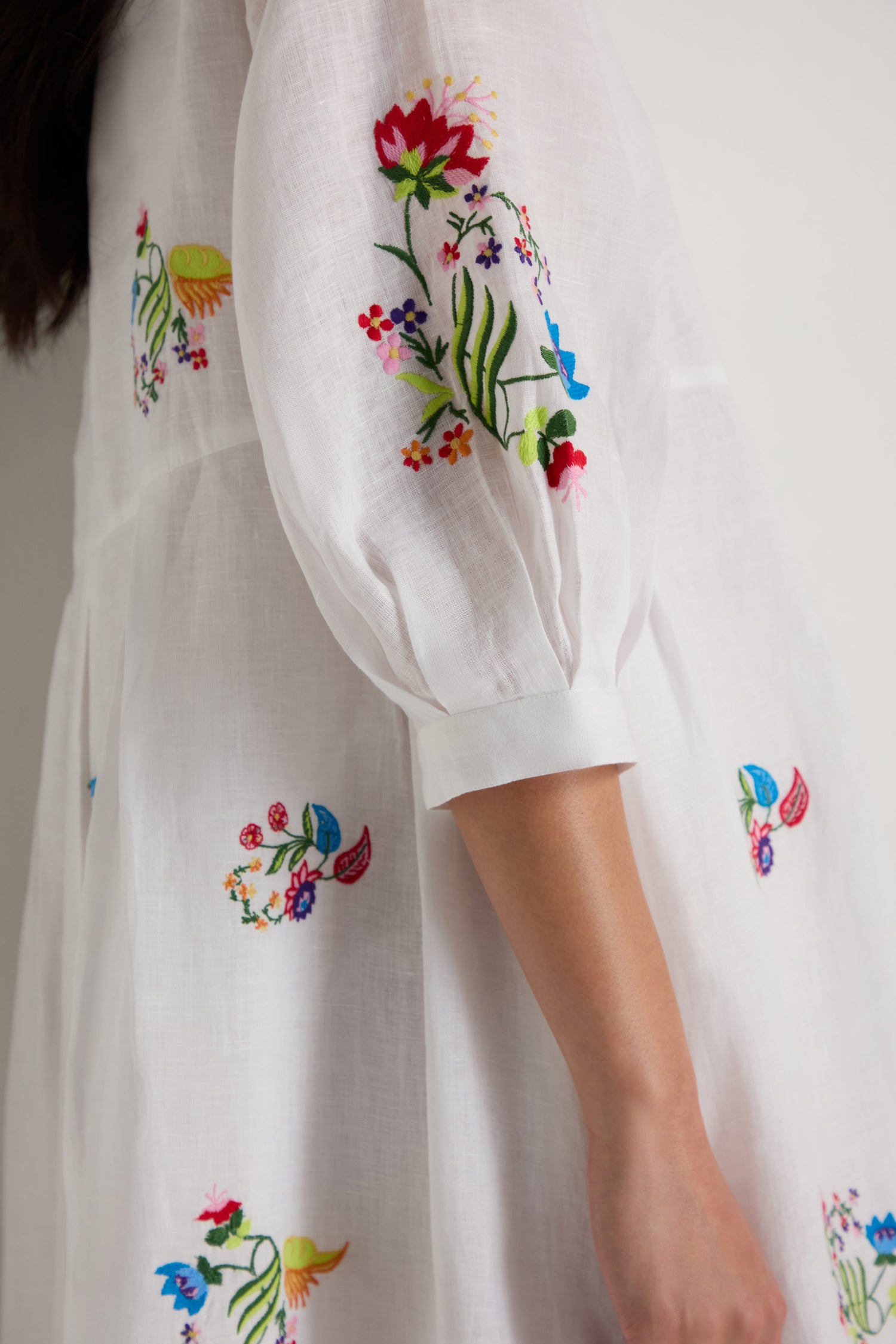 Someone wearing the Vintage Floral Embroidered Flare Dress—a white dress with colorful floral embroidery and three-quarter length puff sleeves.