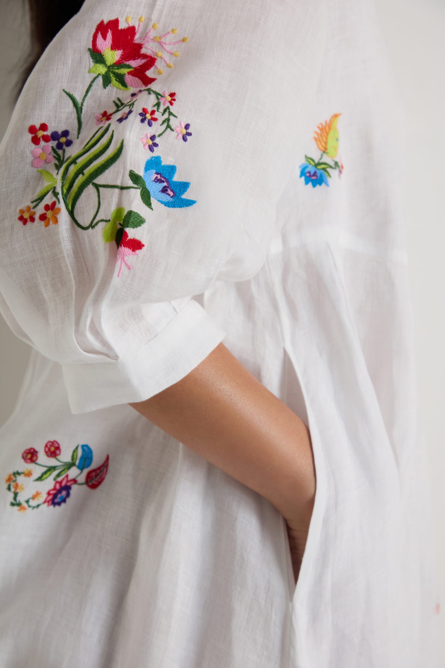 Wearing the Vintage Floral Embroidered Flare Dress, a person shows off colorful floral and bird embroidery on the sleeve and back, with one hand casually tucked into a side pocket.