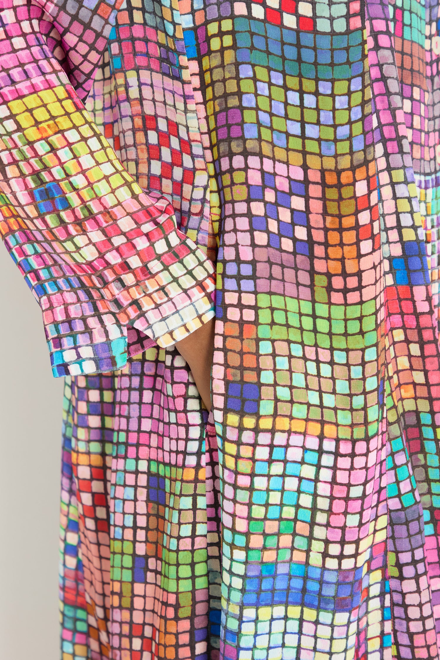 A woman with long brown hair wears the Coloured Glass Tiles Shirt Dress, featuring a vibrant, pixelated geometric pattern in pink, blue, green, and more.
