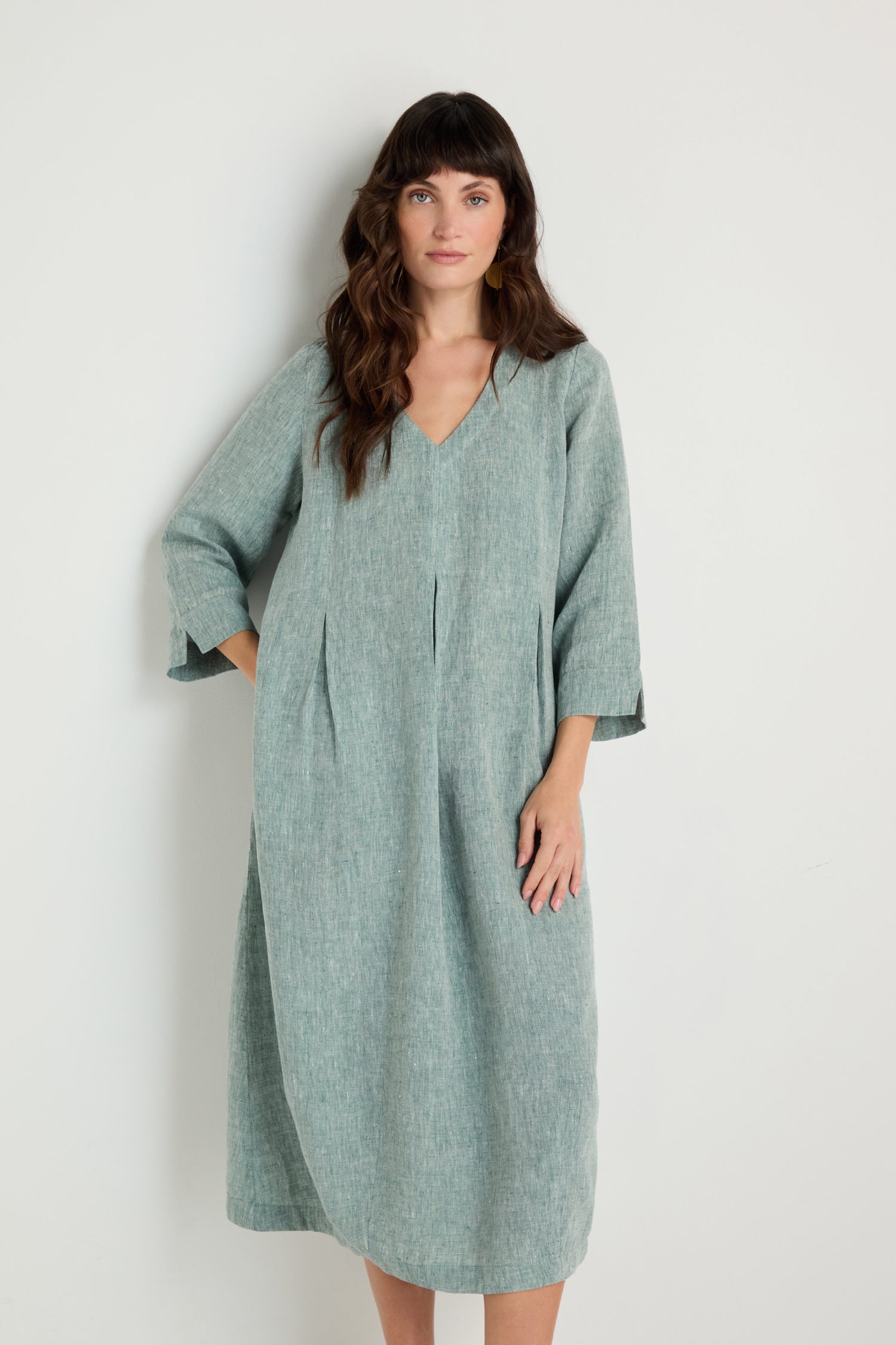 A woman stands against a plain white background wearing the Crinkle Linen Cross Dye Bubble Dress in light green, featuring a loose fit, knee length, and three-quarter sleeves.
