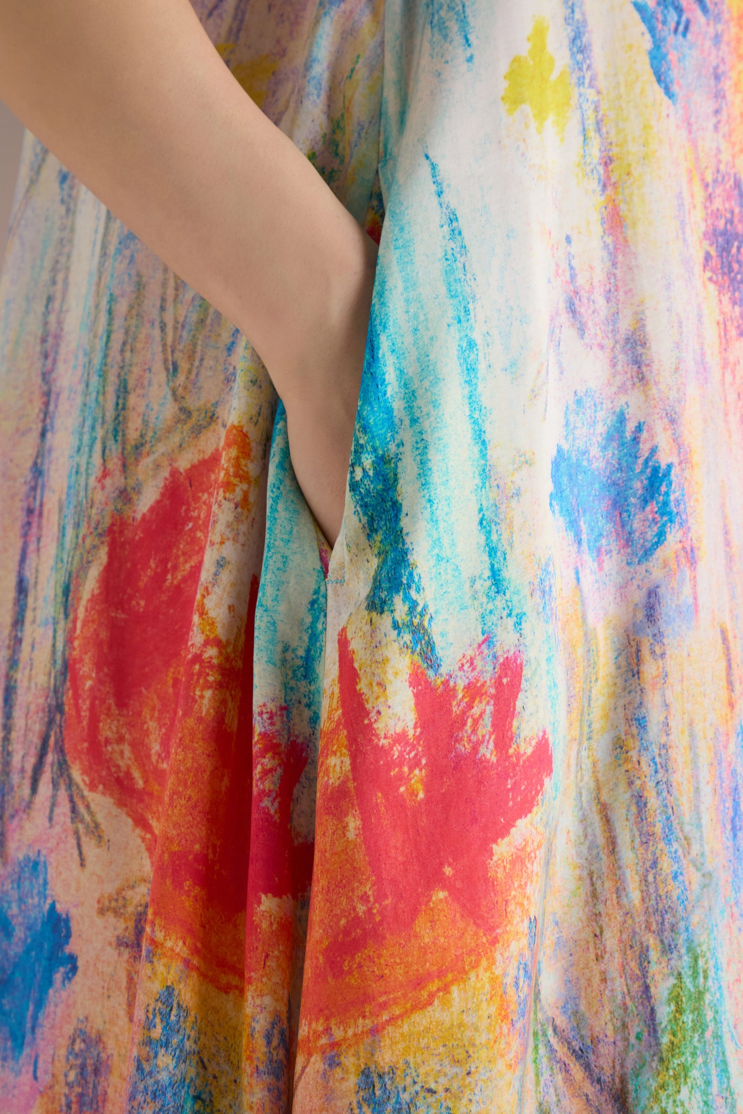 A close-up of a hand in the pocket of the Meadow Dreams Sleeveless Dress, featuring a colorful abstract watercolor pattern in red, blue, yellow, and green.