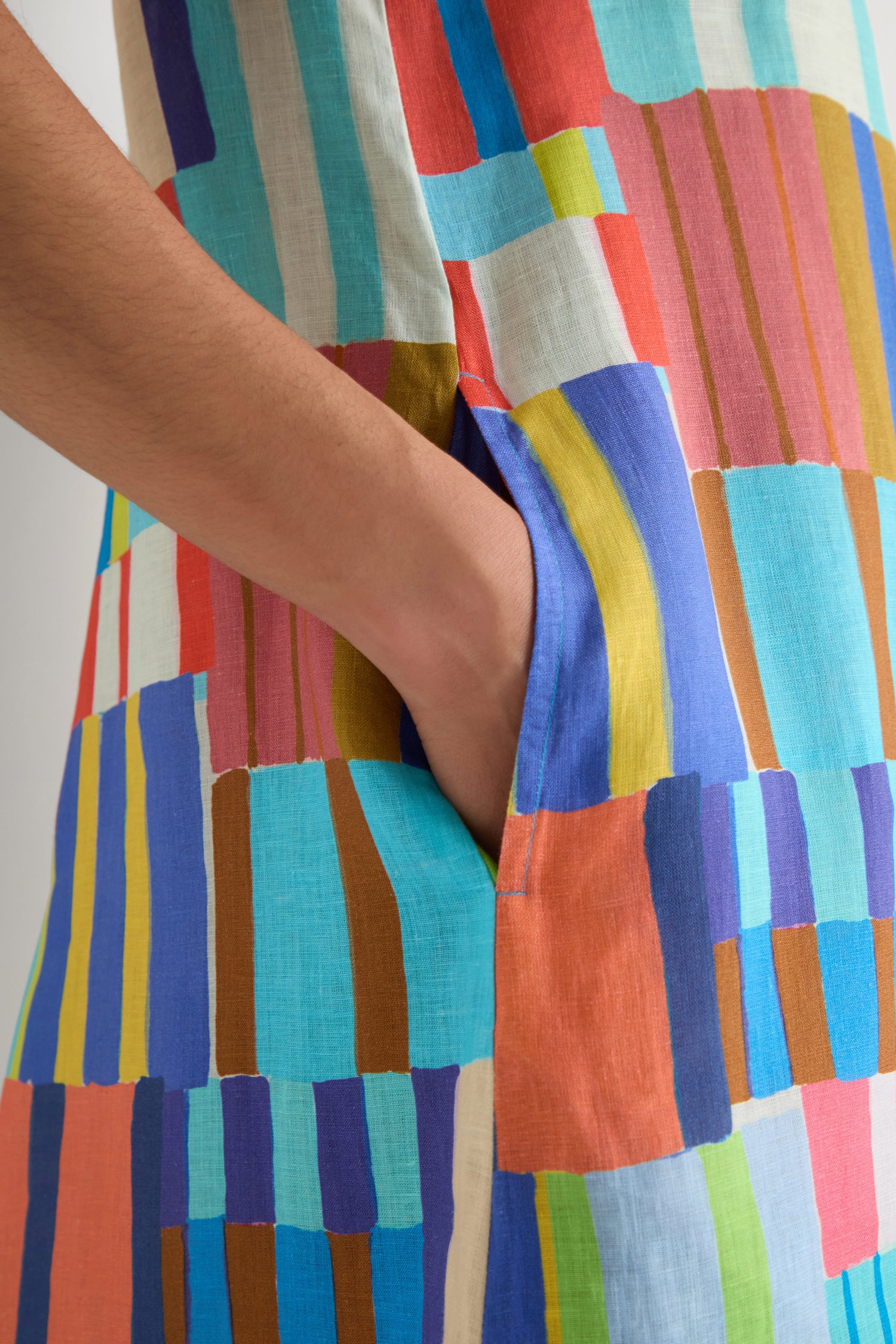 A hand rests in the pocket of the Painted Stripes A-Line Dress, which showcases a vibrant geometric pattern with colorful vertical and horizontal stripes.