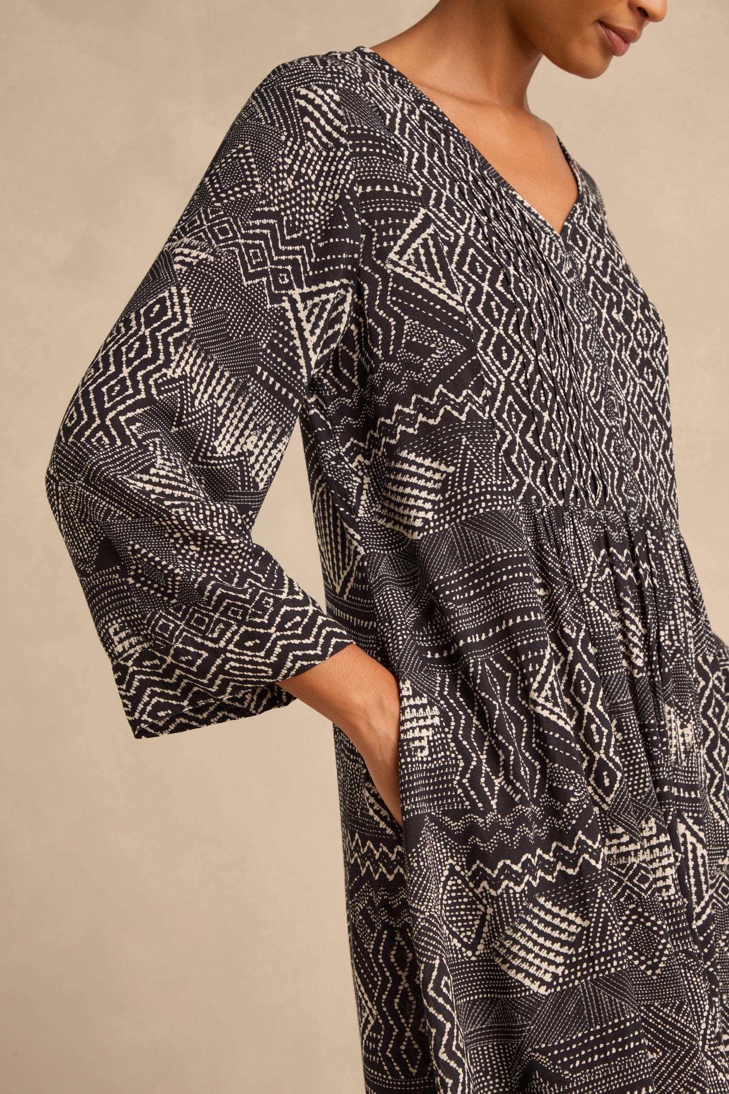A person is photographed from the side, wearing the Mono Patchwork Ikat Dress—a long-sleeved, black and white geometric patterned design with an A-line silhouette and a pocket where one hand rests.