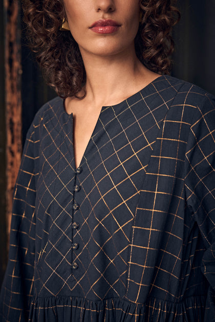 A person wearing a Lurex Check Flared Dress in dark navy with a metallic gold checkered pattern and a buttoned V-neck placket.