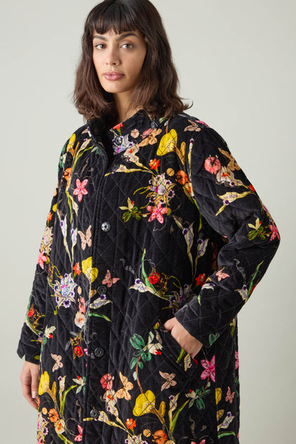 A person wearing a Merino Wool Crop Jumper adorned with a colorful floral pattern stands against a plain background, the vibrant turquoise accents catching the eye.