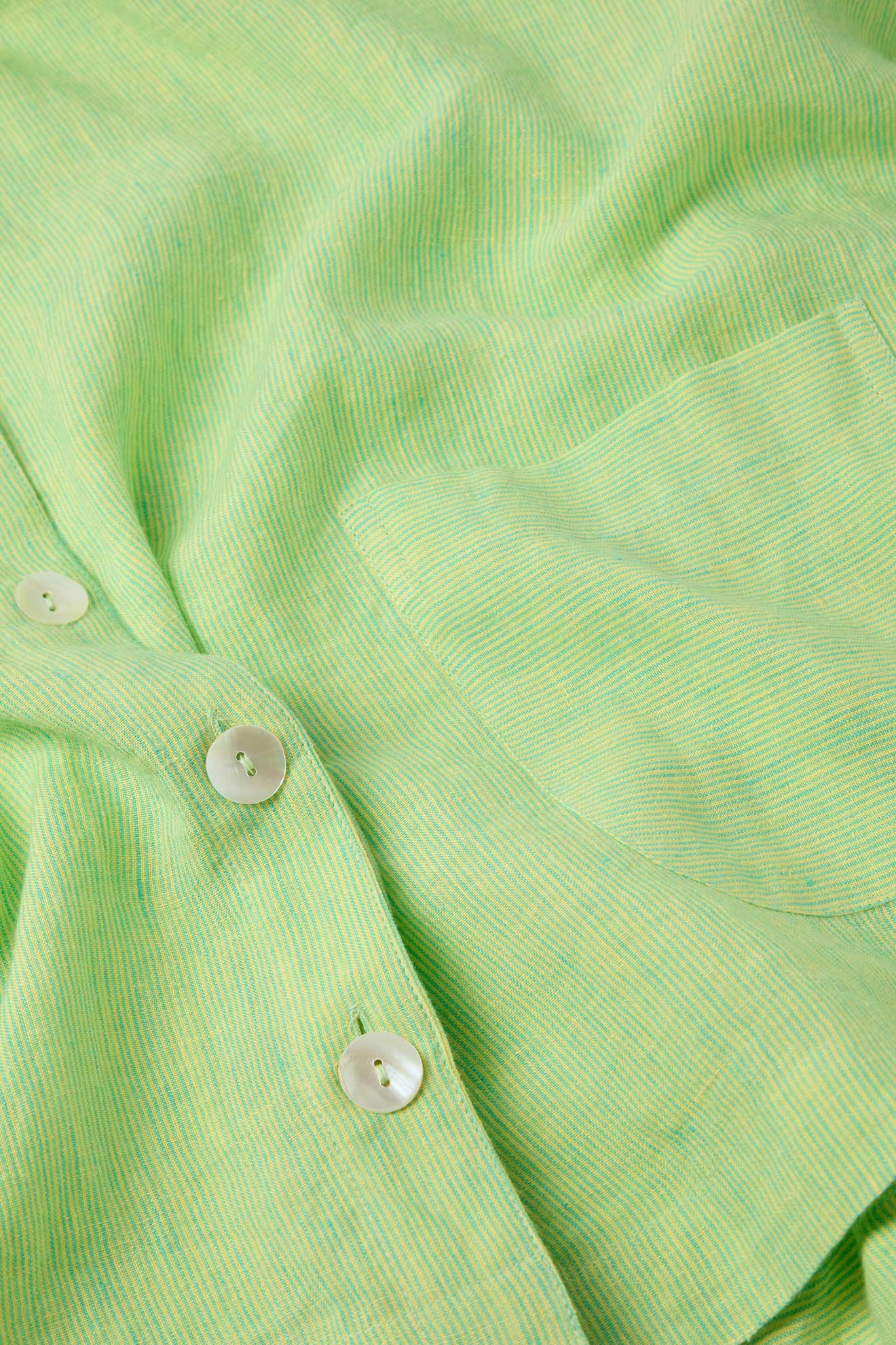 Close-up of the Linen Ticking Stripe Boxy Jacket, highlighting its green fabric with a pocket and white buttons, showcasing the texture and detailed craftsmanship of the material with its subtle ticking stripe pattern.