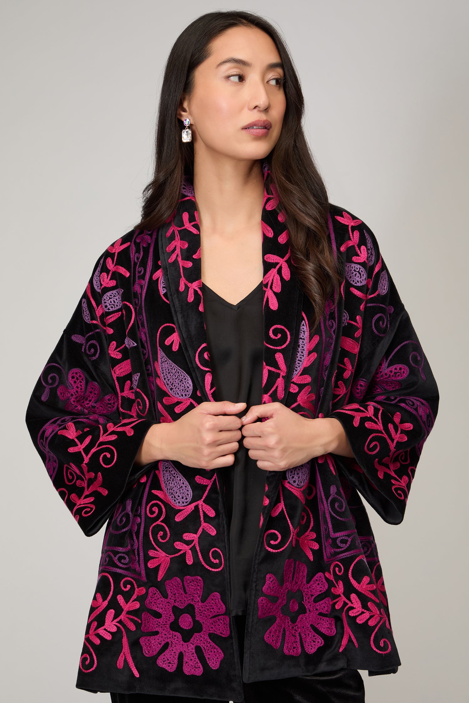 A woman with long dark hair models the Winter Embroidered Jacket, featuring black and magenta floral embroidery, over a black outfit against a plain background—ideal for stylish winter wear.